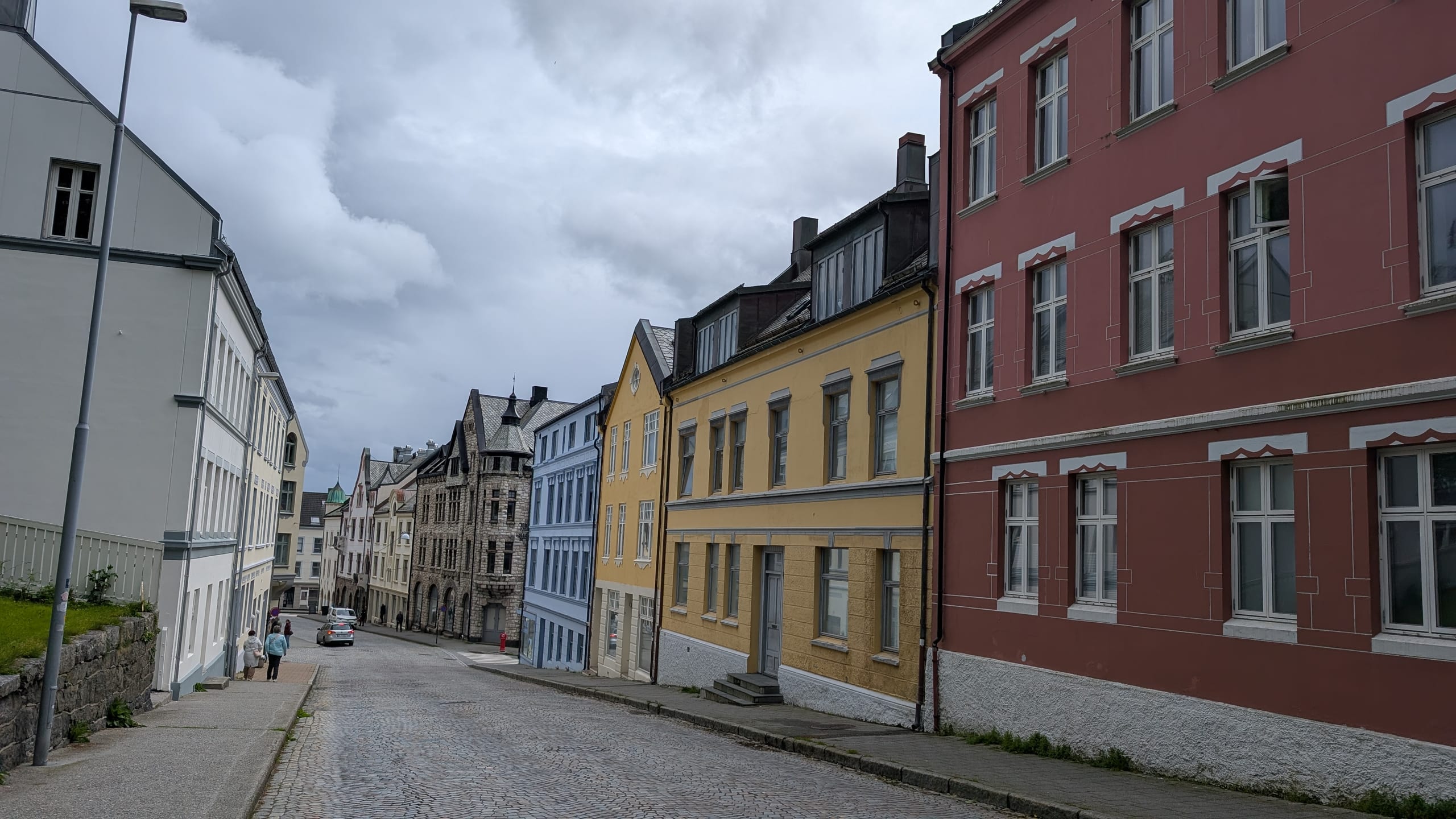 Art Nouveau facades in terracotta, yellow, and grey lining a sloping cobblestone street in Ålesund