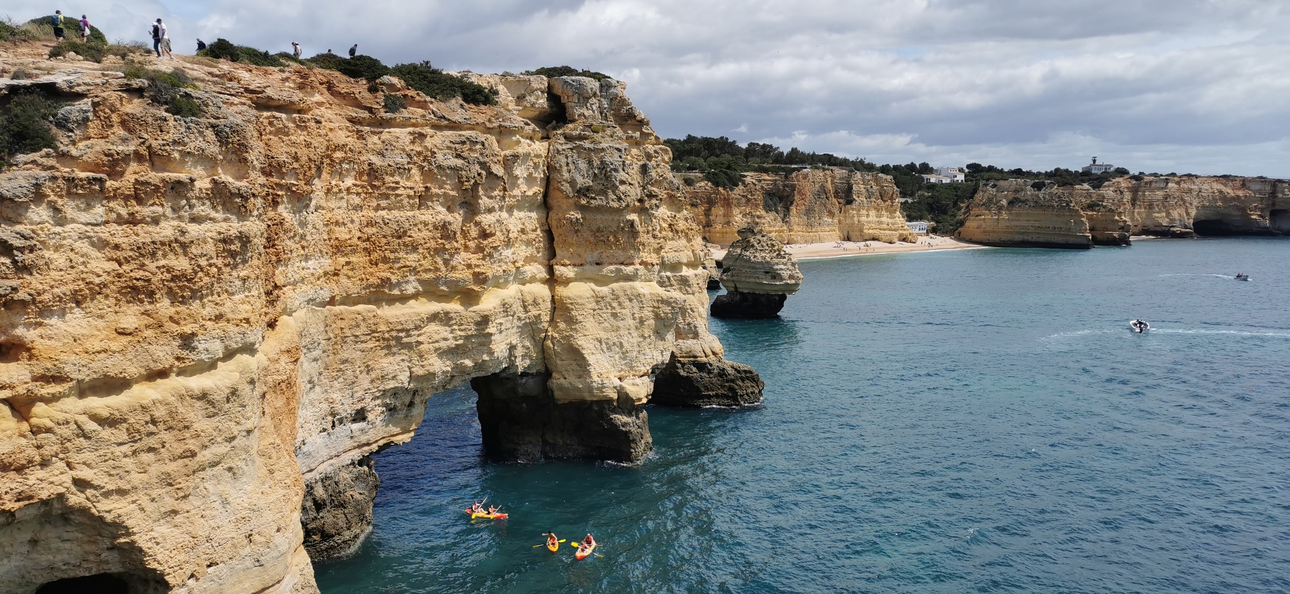 Yellow and orange kayaks beside a natural limestone arch on the cliffs between Praia da Marinha and Benagil
