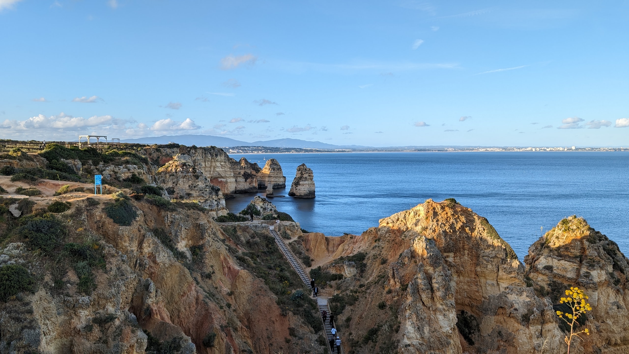 Ochre limestone cliffs and sea stacks at Ponta da Piedade near Lagos, with a wooden staircase dropping toward the Atlantic