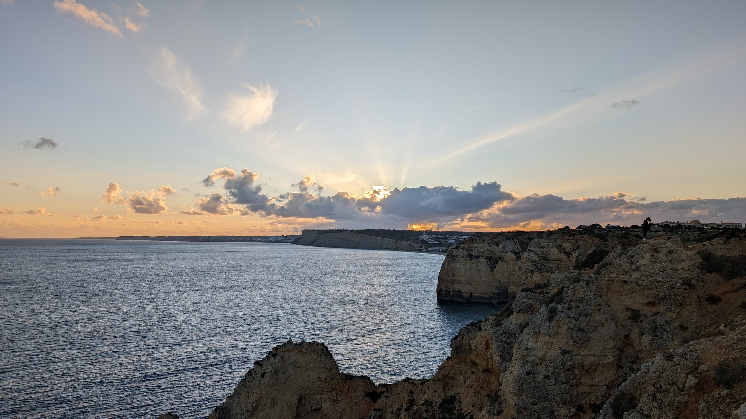 Late sun breaking through cloud over ochre limestone cliffs at Ponta da Piedade, with a person standing on the headland