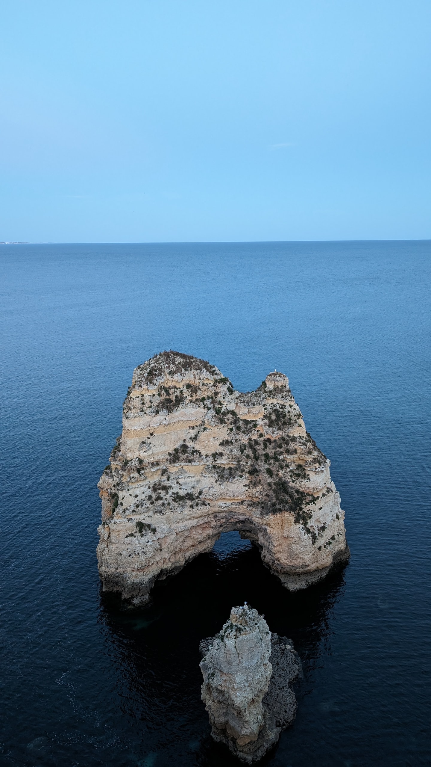 A weathered limestone sea stack with a natural arch at its base in deep blue water off the Lagos coast