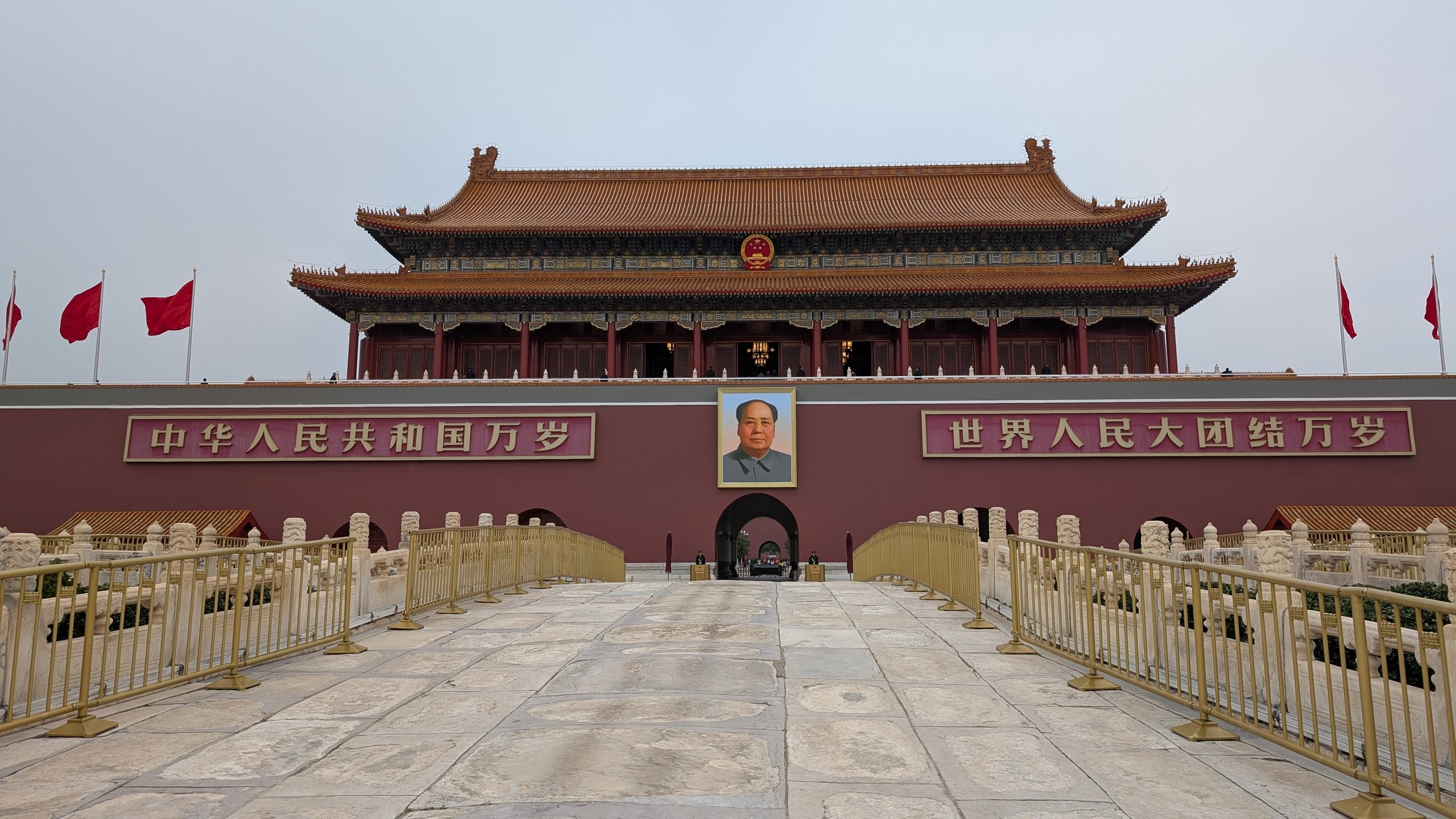 The Gate of Heavenly Peace in Beijing with red flags, Mao's portrait, and barriers across the stone approach