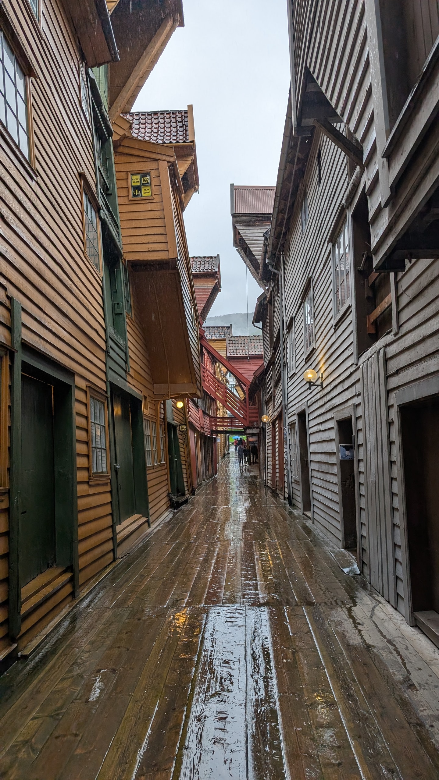 A narrow wet wooden alley between Hanseatic warehouses in Bryggen, with overhanging floors and red bridges linking the upper stories