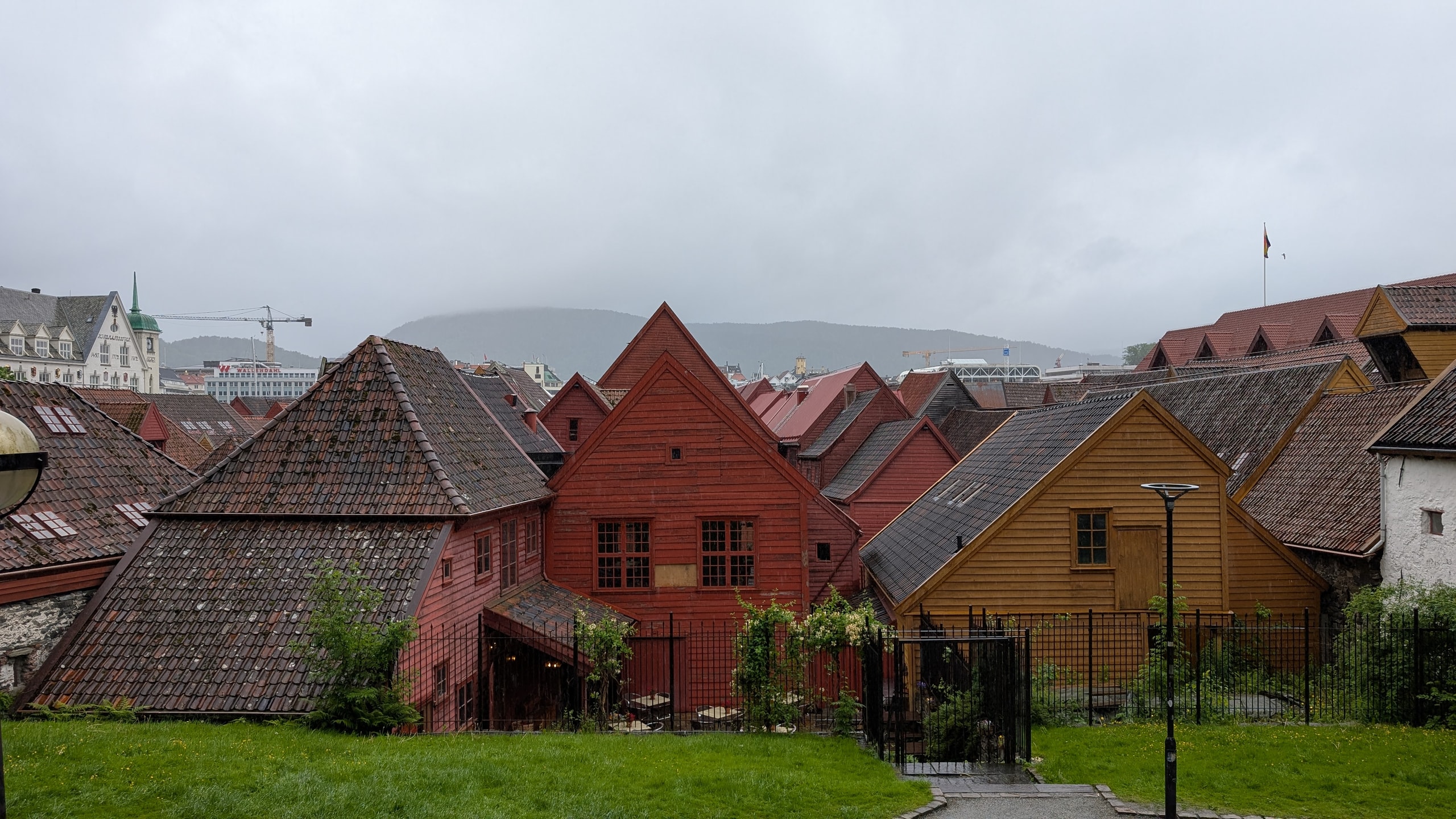 Looking down over Bryggen’s red and yellow wooden rooftops from a grassy hillside, with mist covering the mountains beyond