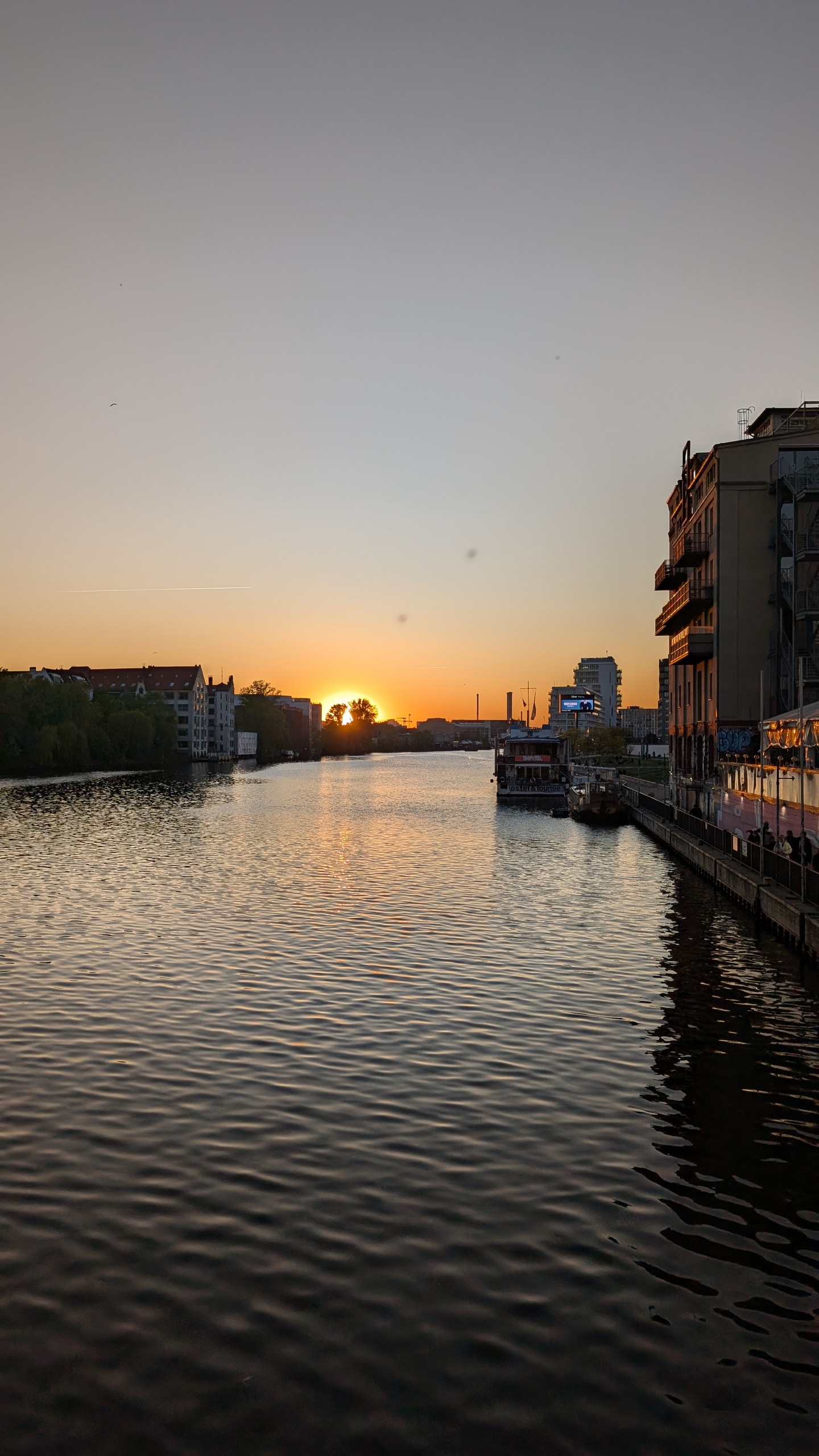 The Spree river at sunset seen from a bridge, orange sky low over the water with apartment buildings and a moored boat along the right bank
