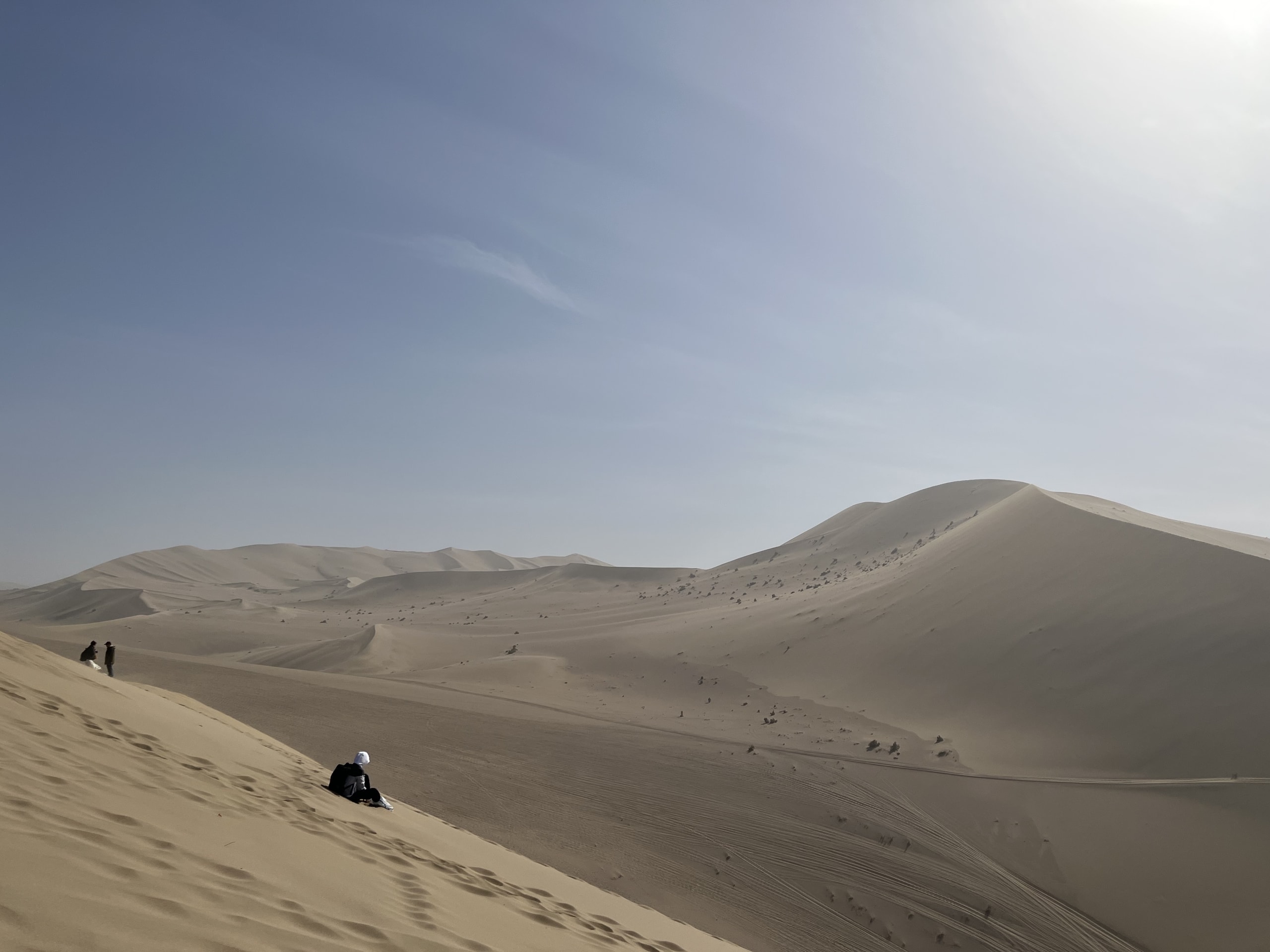 Sand dunes near Dunhuang with footprints on a steep slope and layered desert ridges under a pale sky
