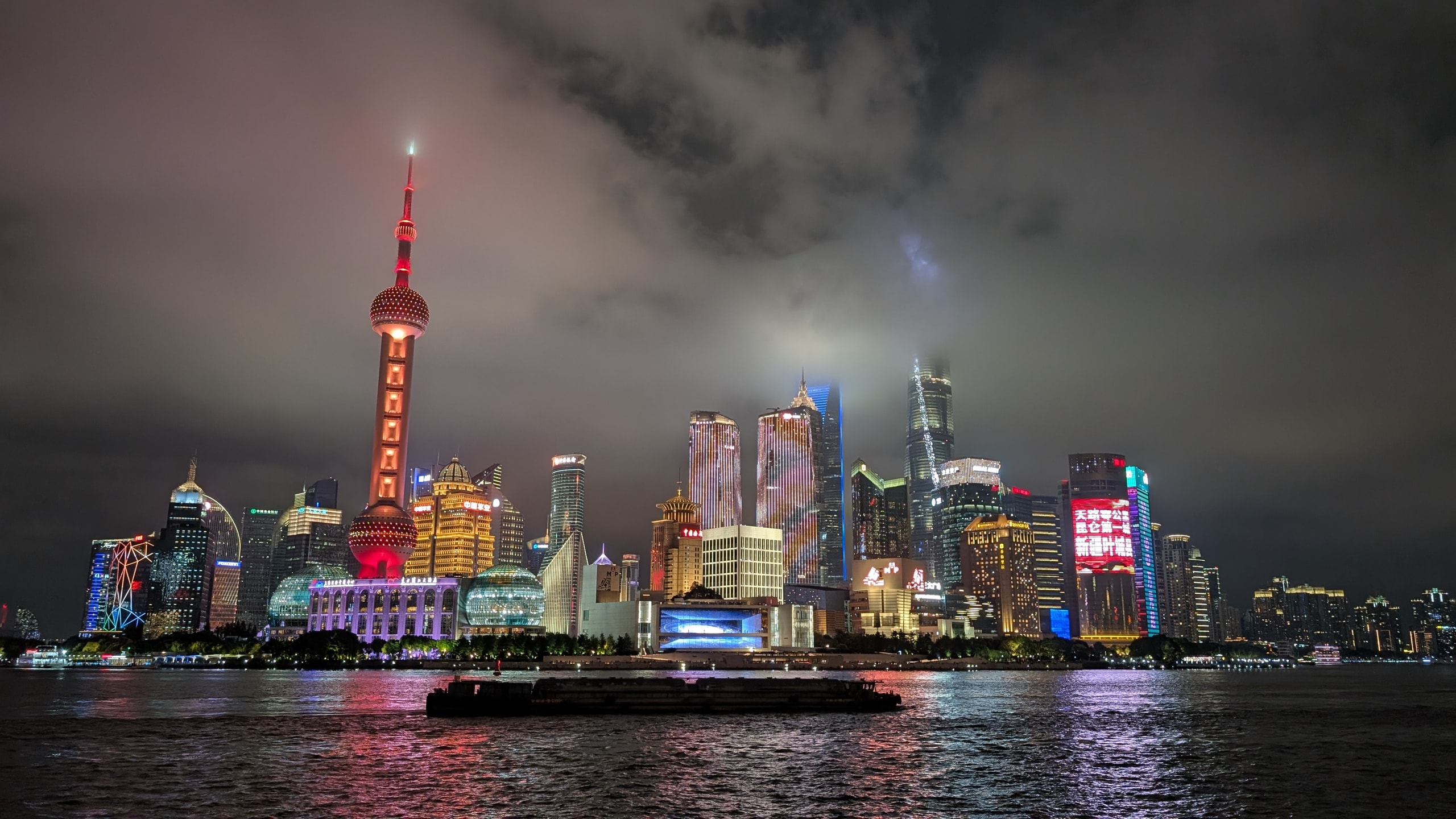Shanghai's Pudong skyline at night across the Huangpu River with the Oriental Pearl Tower lit red and white