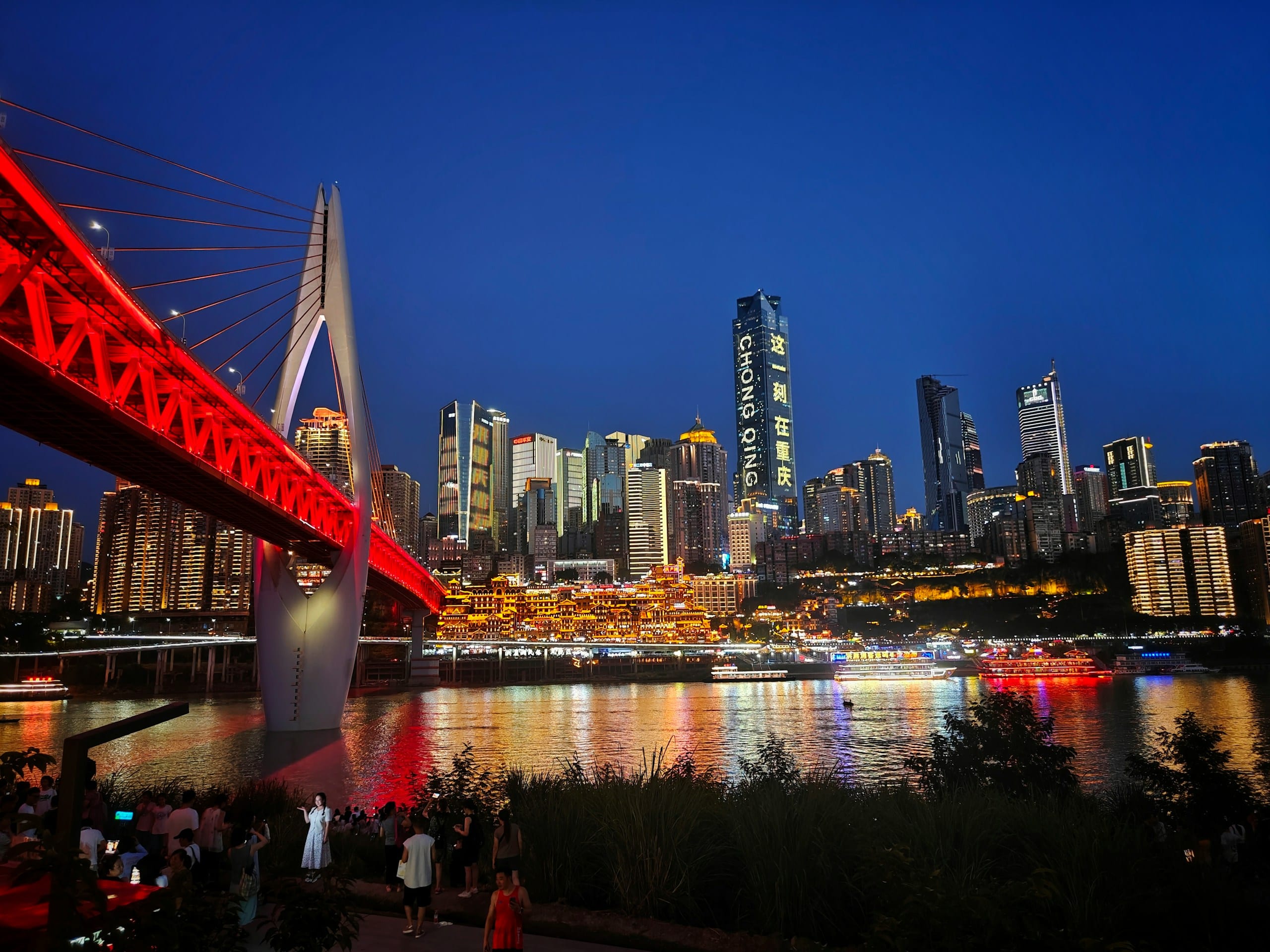 Chongqing nighttime skyline with illuminated towers and a bright red bridge spanning the river