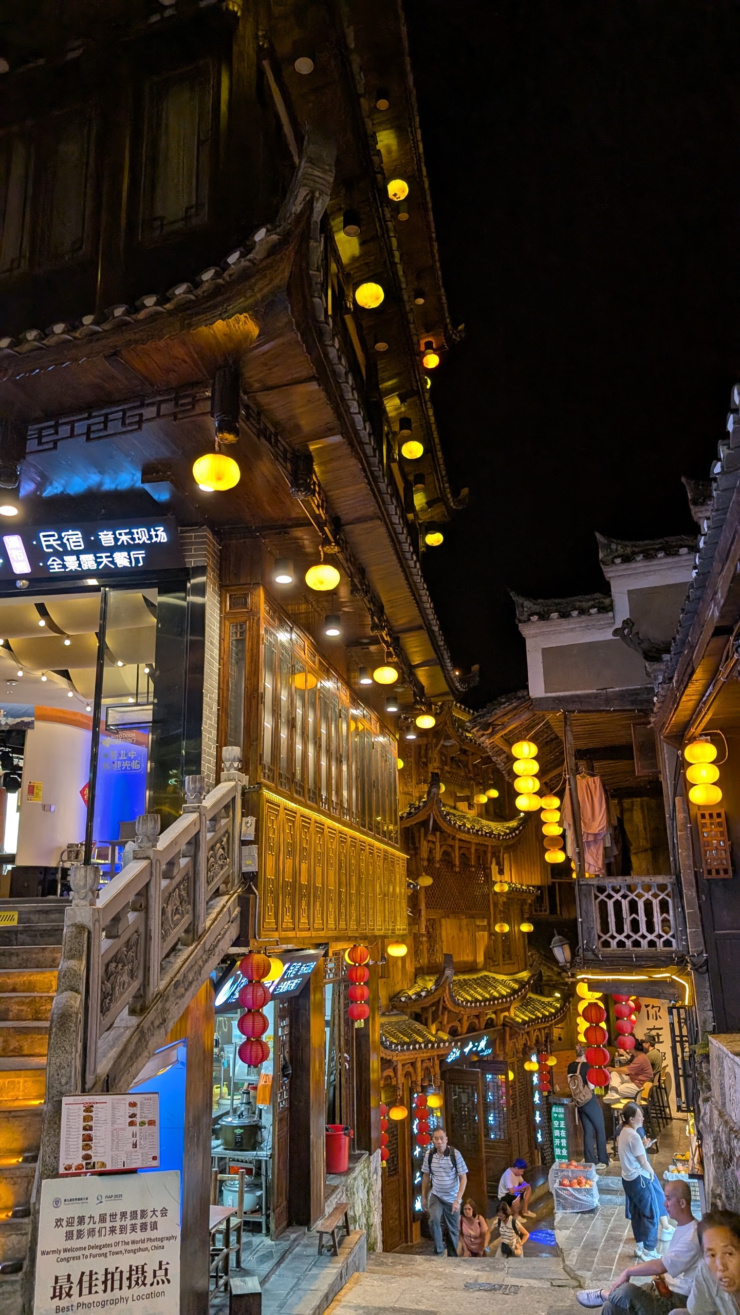 Stone staircase with carved banister leading up a lantern-lit street in Furong Ancient Town past wooden shopfronts