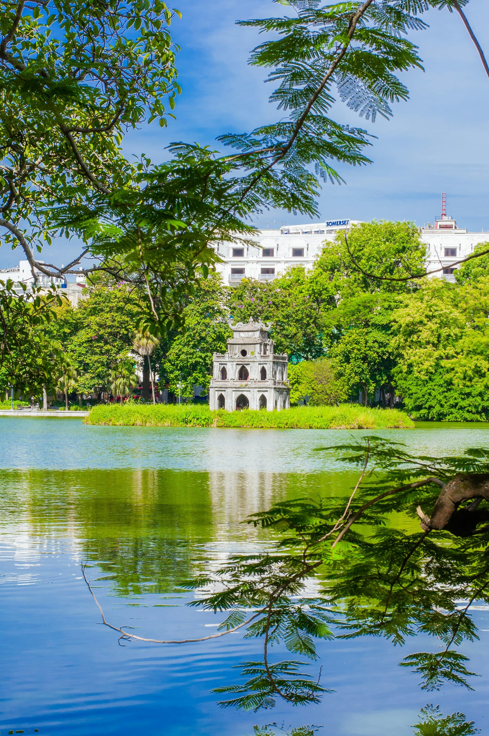 Hoan Kiem Lake in Hanoi with trees along the shore and a tower visible across the water