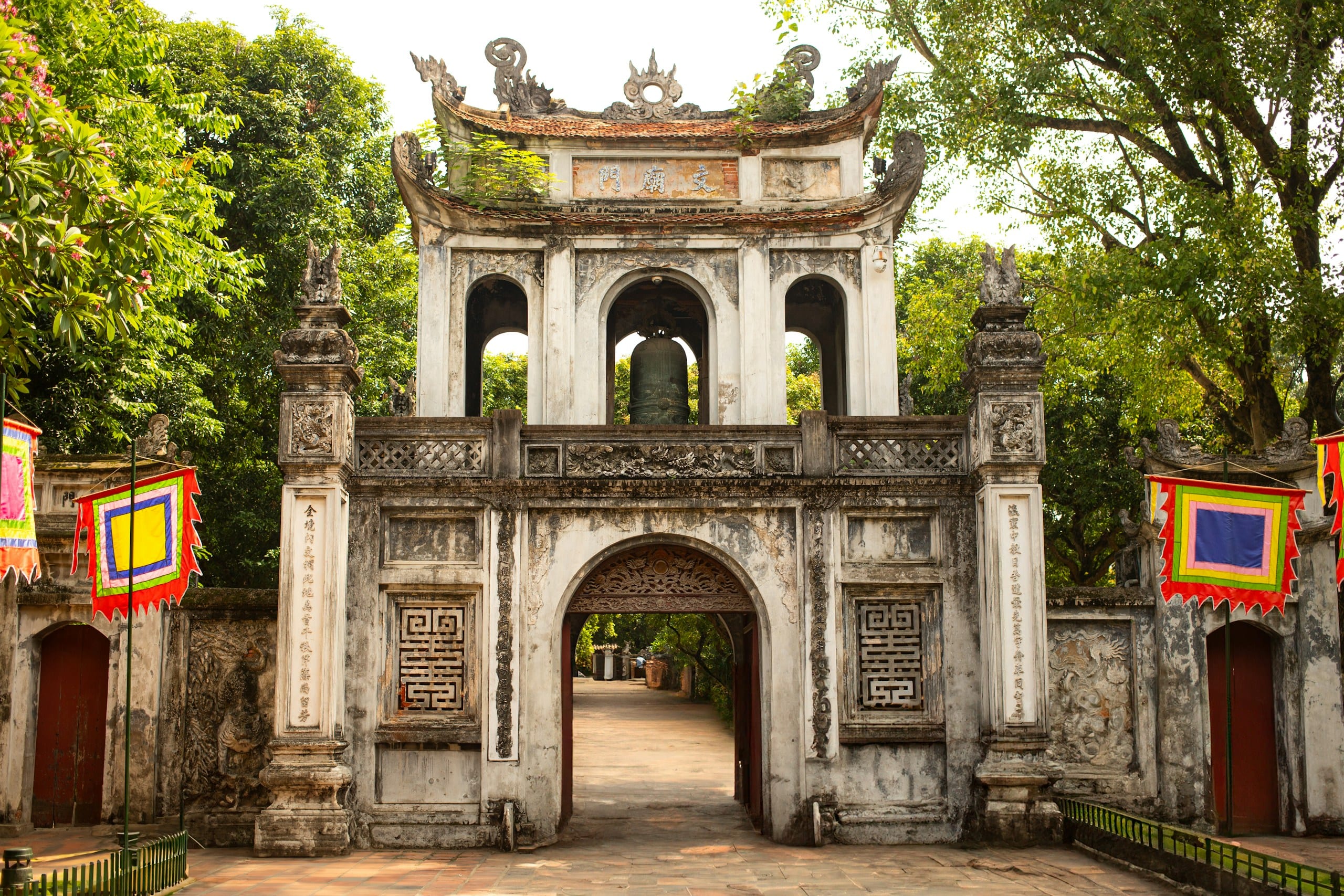 The ornate stone entrance gate to the Temple of Literature in Hanoi with red flags