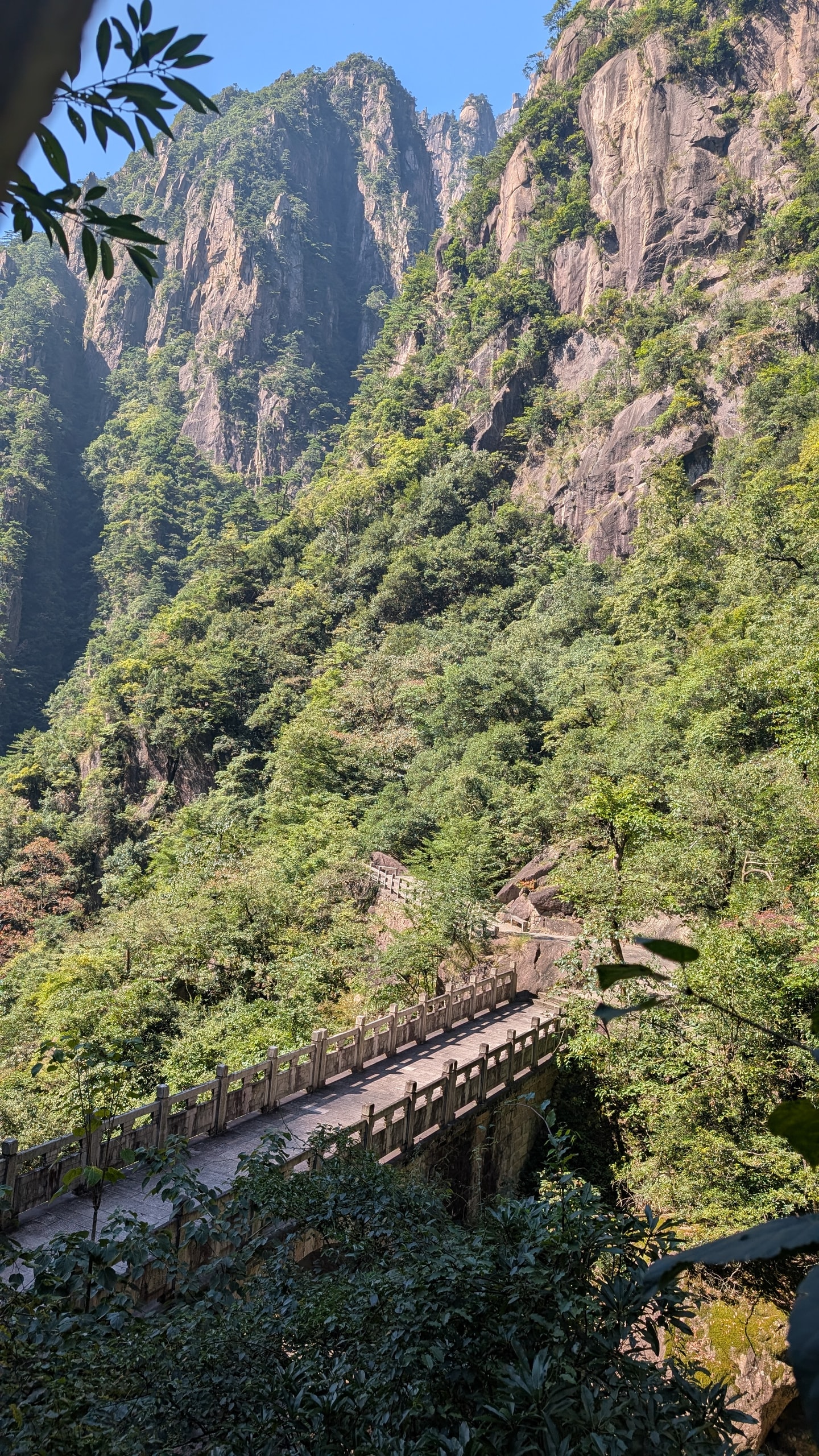 Stone bridge with square railings spanning a green ravine between steep Huangshan granite cliffs