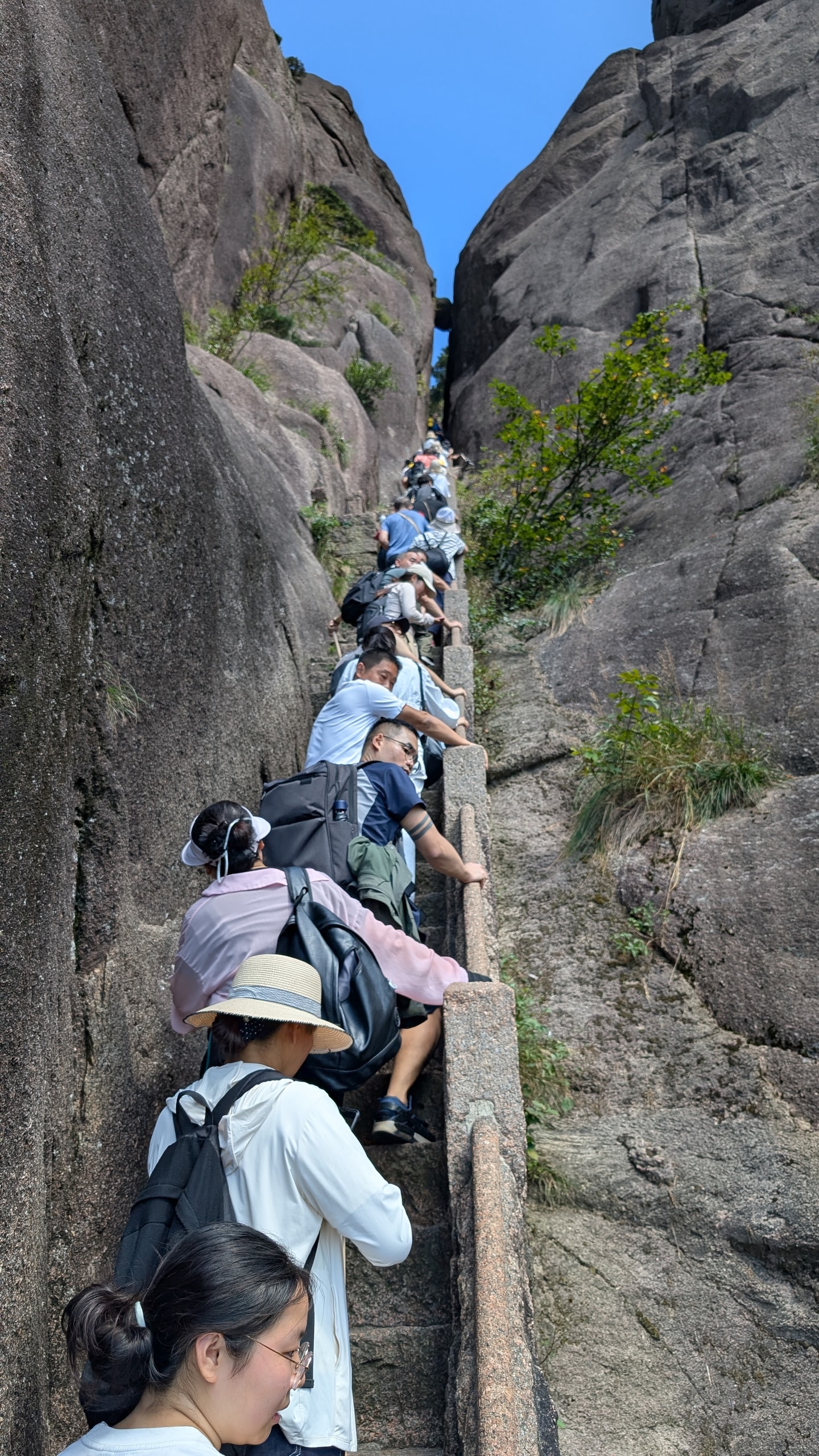 Line of hikers ascending a steep stone staircase wedged between towering granite walls on Huangshan