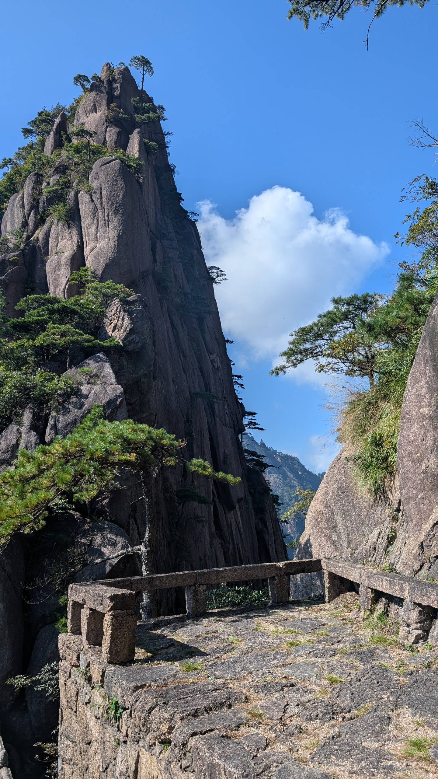Stone viewing platform on Huangshan looking between granite peaks toward a white cloud and blue sky