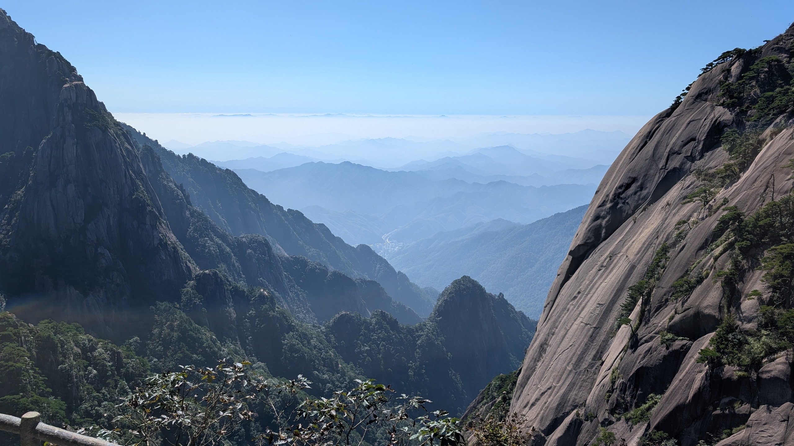Deep Huangshan valley framed by granite peaks with distant ridges fading into haze under a clear blue sky