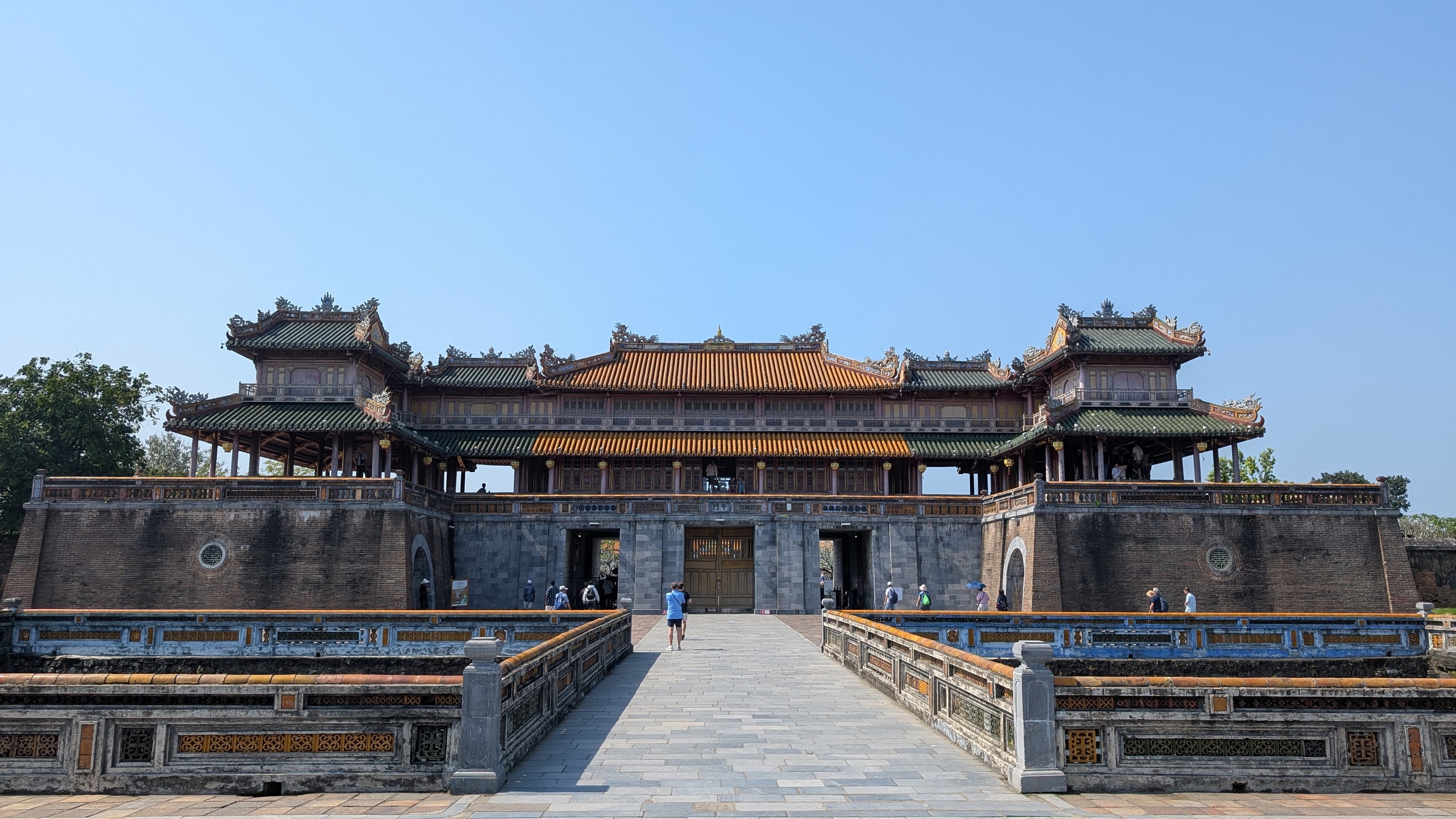 The Noon Gate of Hue's Imperial City, a stone base with five doorways under a two-storey wooden pavilion with orange and green tiled roofs, reached by a stone bridge