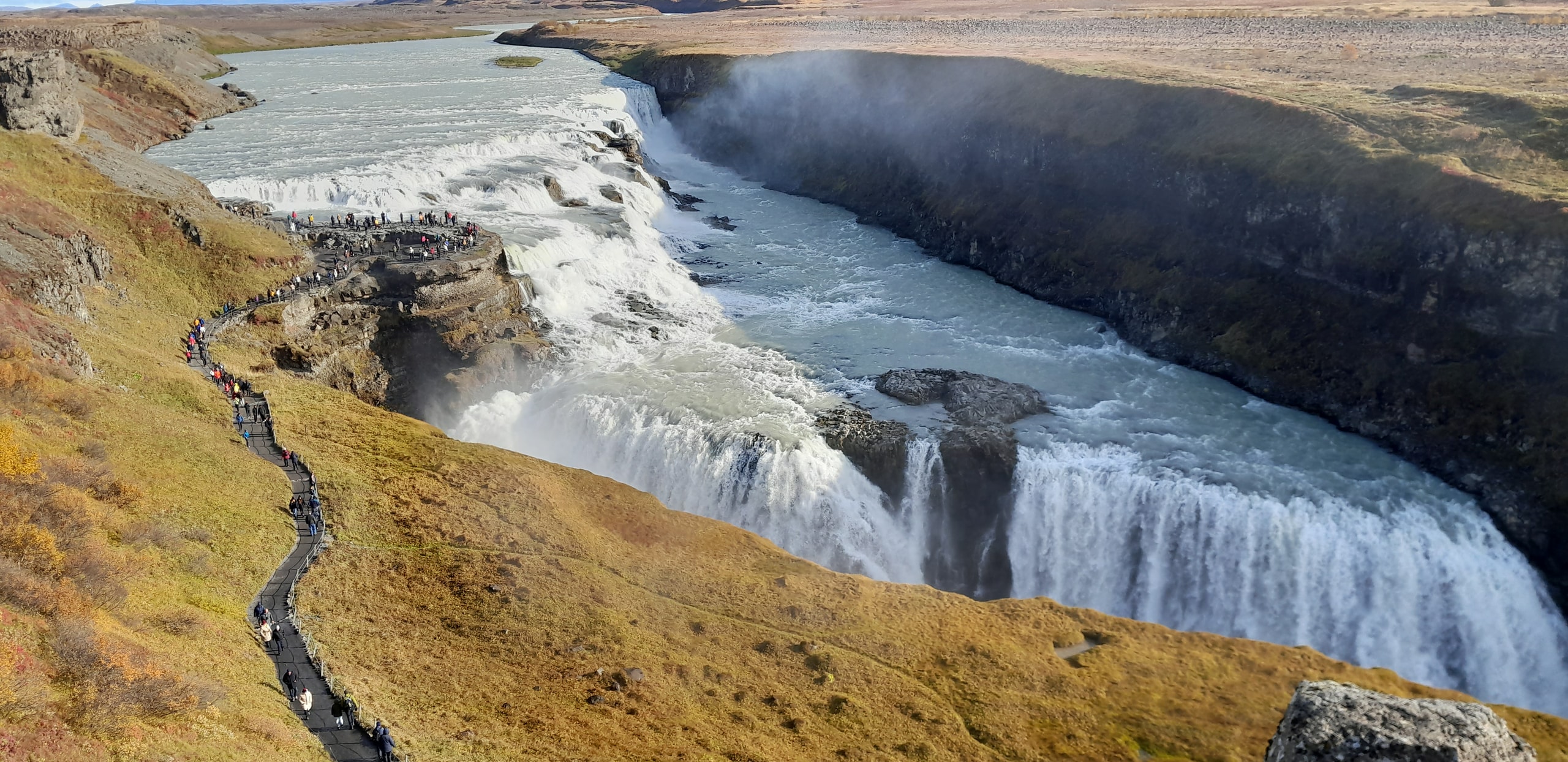 Gullfoss waterfall dropping into a deep canyon with mist rising and a path of visitors along the rim