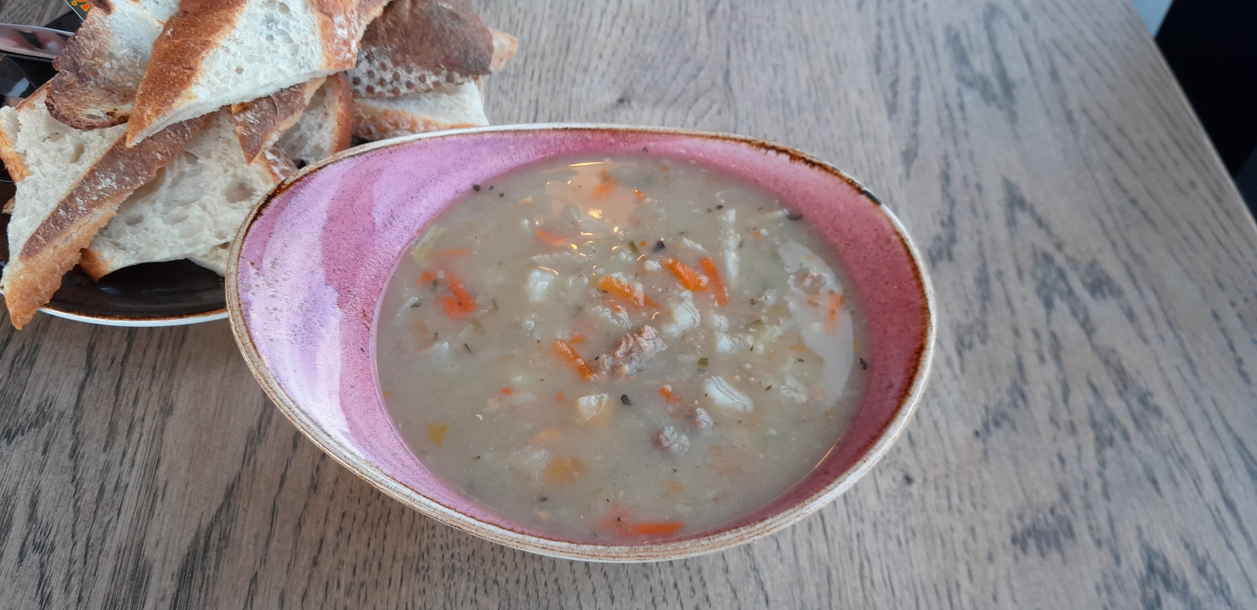 A ceramic bowl of Icelandic lamb soup with carrots and root vegetables beside sliced rustic bread on a wooden table