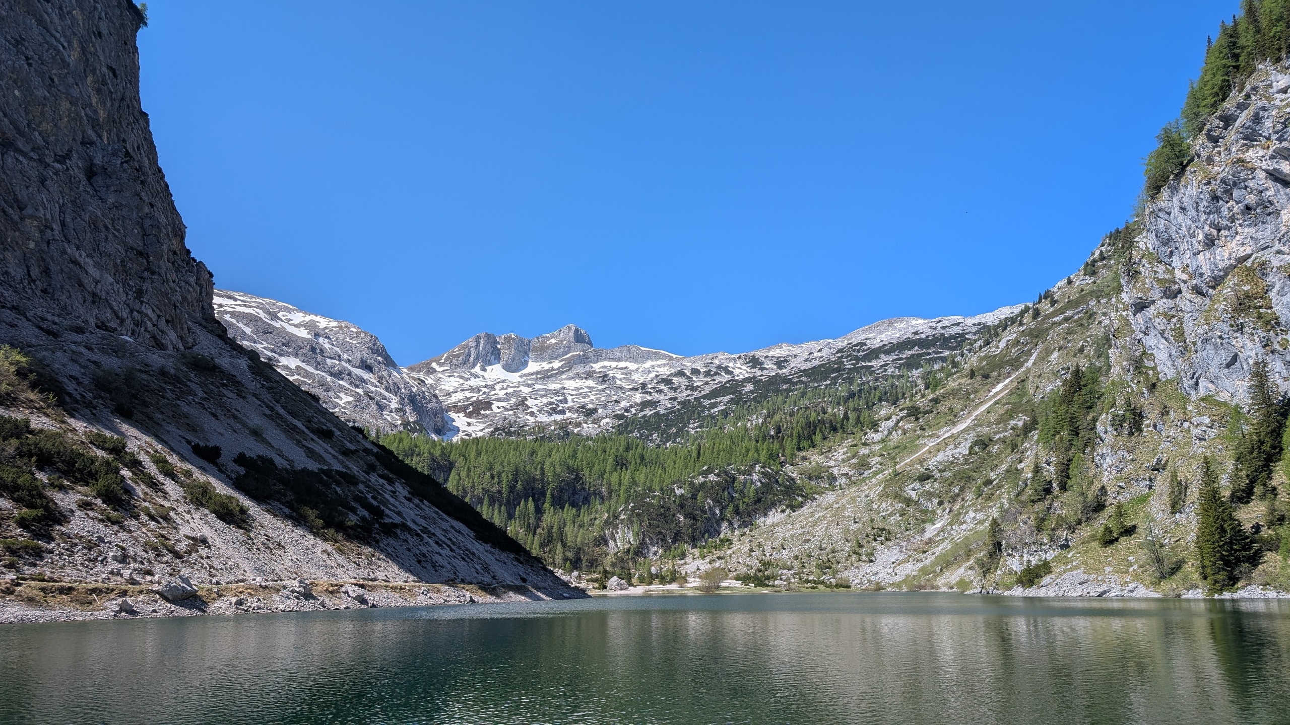 Turquoise Krn Lake ringed by forest and limestone peaks with late-spring snow in the Julian Alps