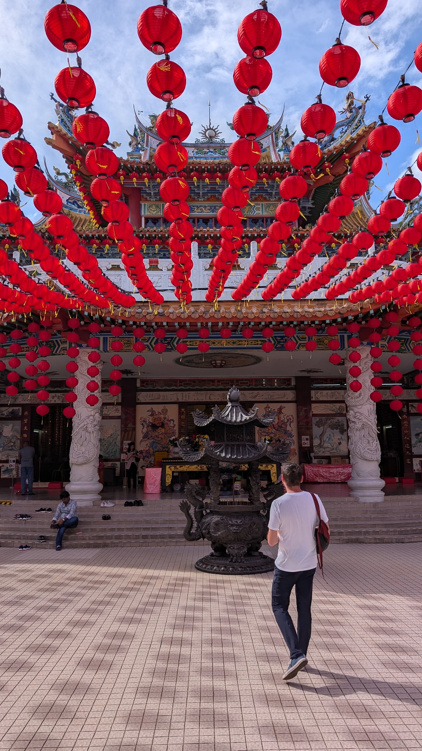 Rows of red lanterns hanging over the main courtyard of Thean Hou Temple, a bronze incense burner in the middle and a visitor walking toward the prayer hall