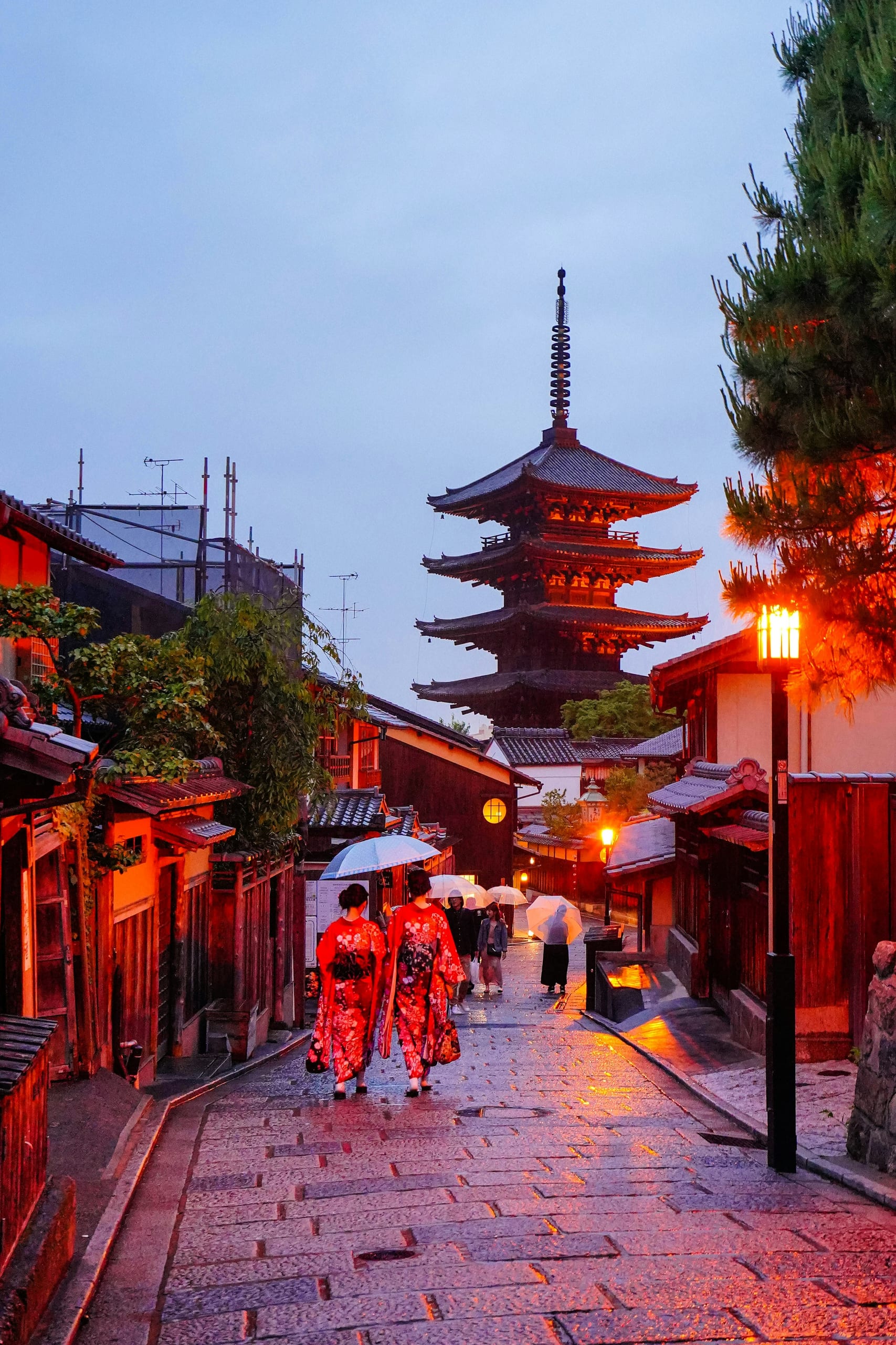 Wet stone street in Kyoto's Higashiyama district at dusk with Yasaka Pagoda ahead and wooden machiya houses on both sides