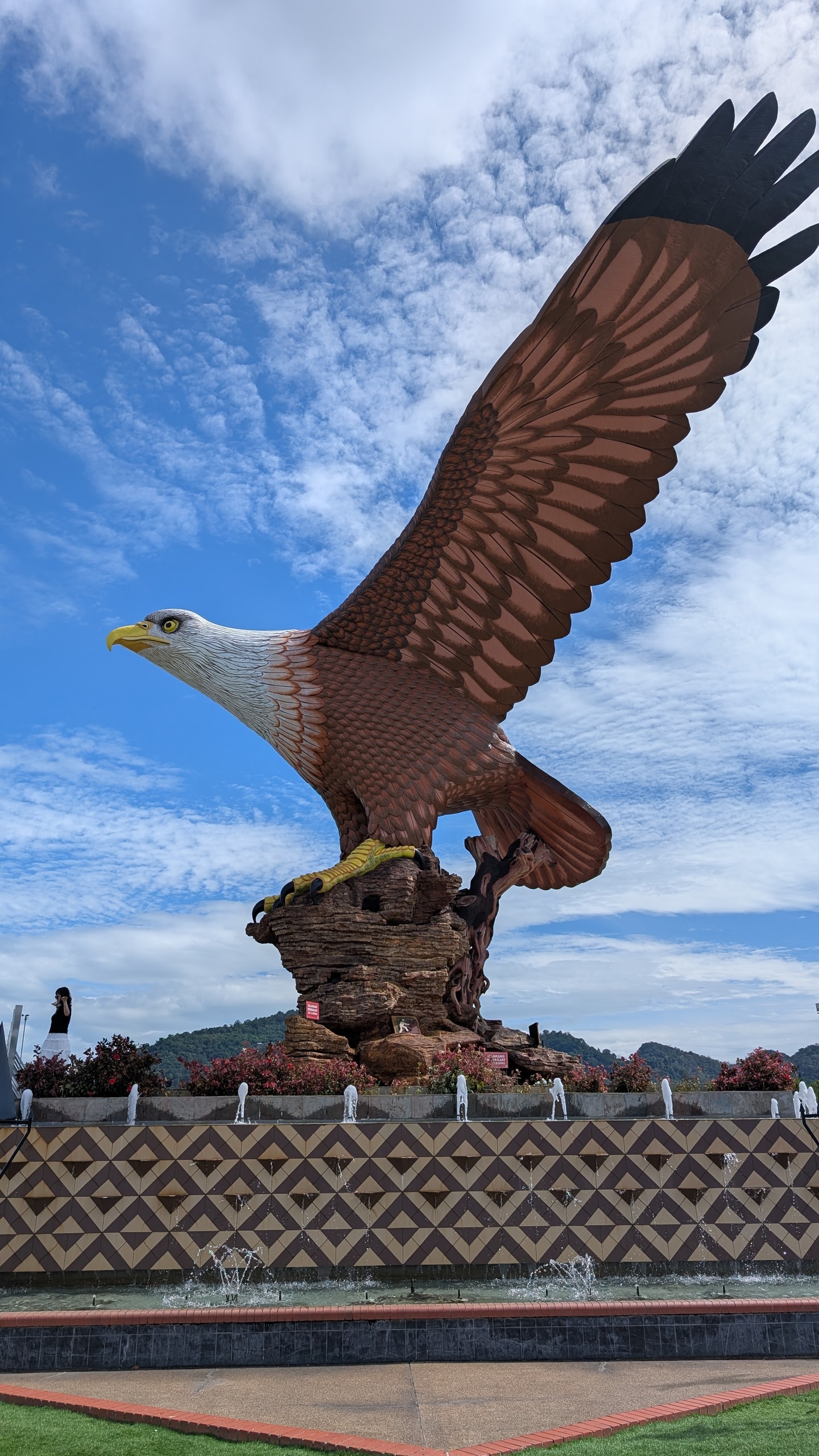 The large reddish-brown eagle statue at Dataran Lang in Kuah, wings raised against a blue sky with fountains below
