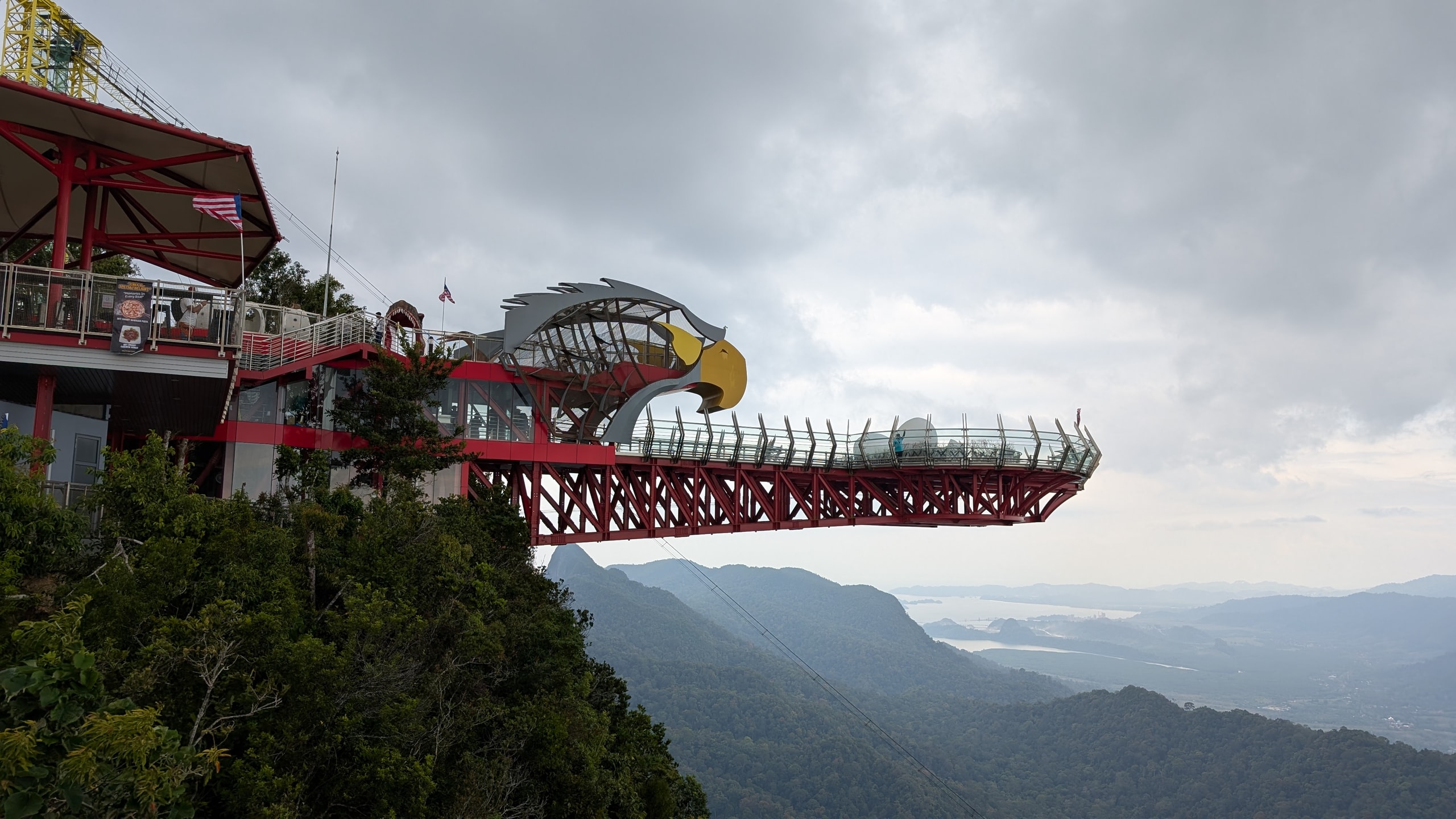 The curved Langkawi SkyBridge with its eagle-shaped station cantilevered over forested mountains under heavy grey cloud