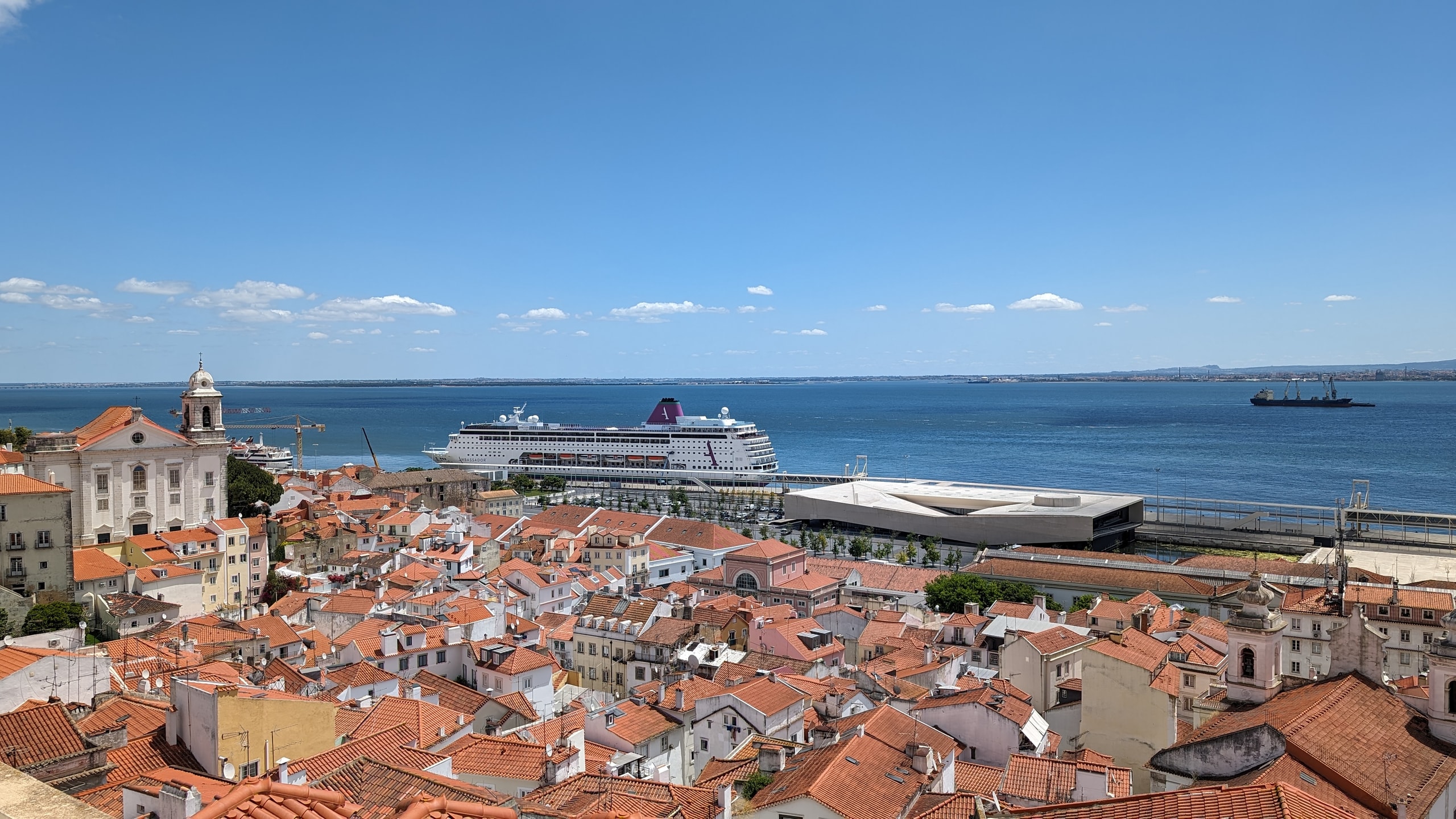 Terracotta rooftops of Alfama dropping to the Tagus, with the white tower of Santo Estêvão and a docked cruise ship