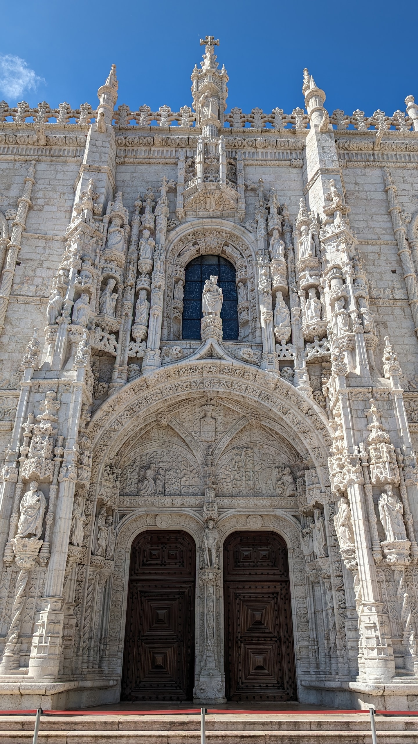 The carved Manueline south portal of Jerónimos Monastery, packed with saints, pinnacles and a central statue of the Virgin, against a blue sky