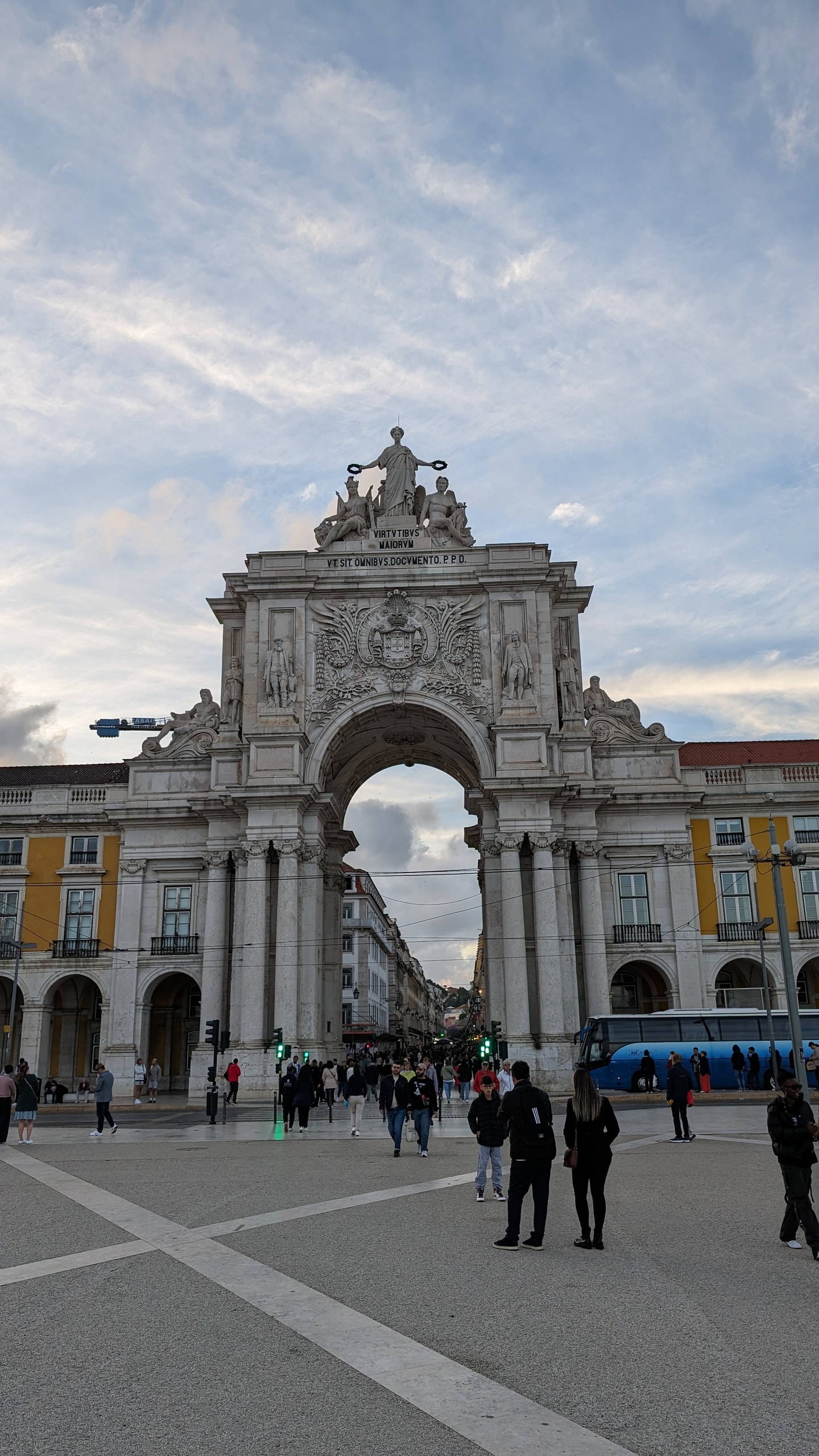 The Rua Augusta Arch on Praça do Comércio, topped with sculptures of Glory, Valor and Genius, with people crossing the square below