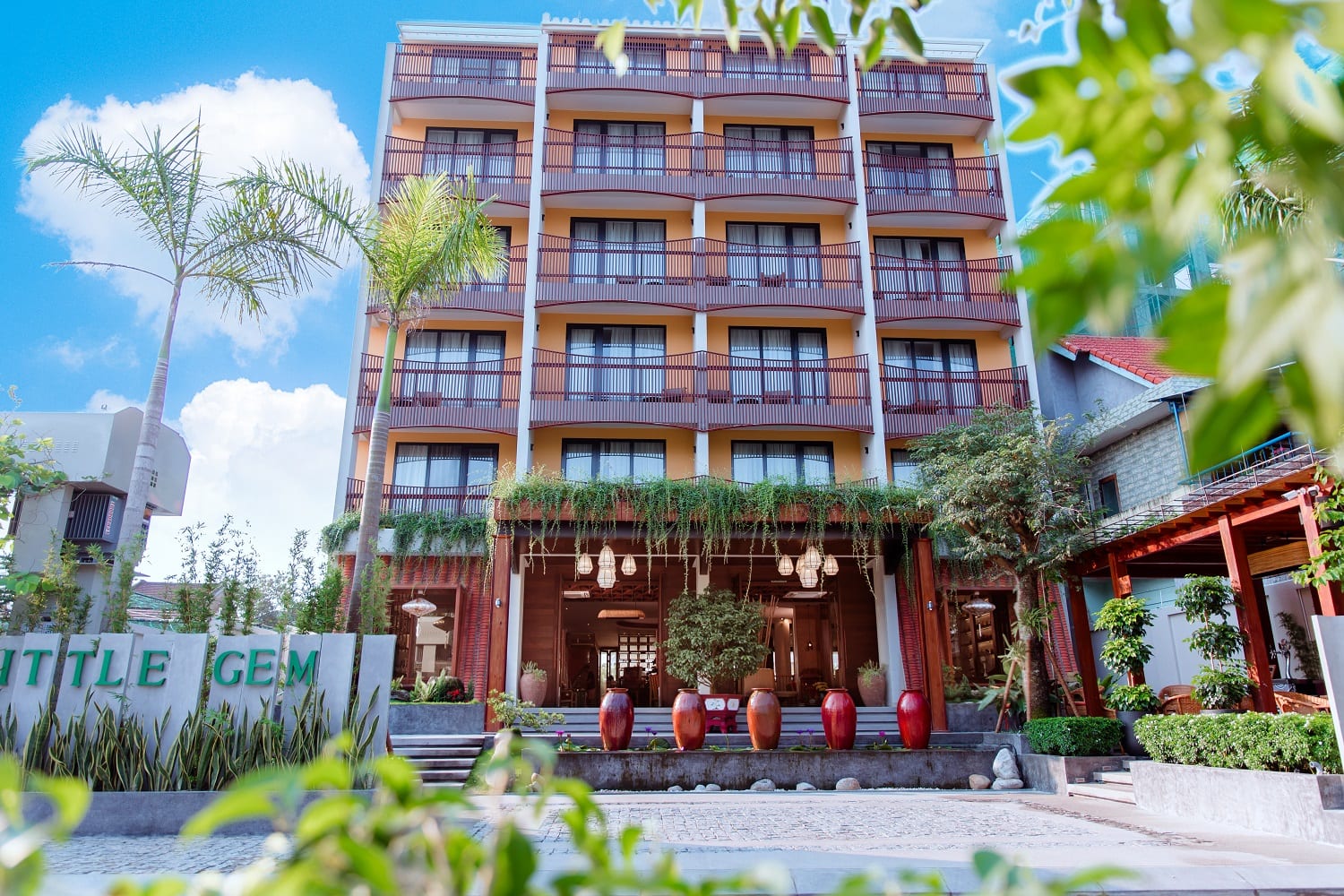 Exterior of Little Gem Hoi An boutique hotel with tropical landscaping along the riverbank approach