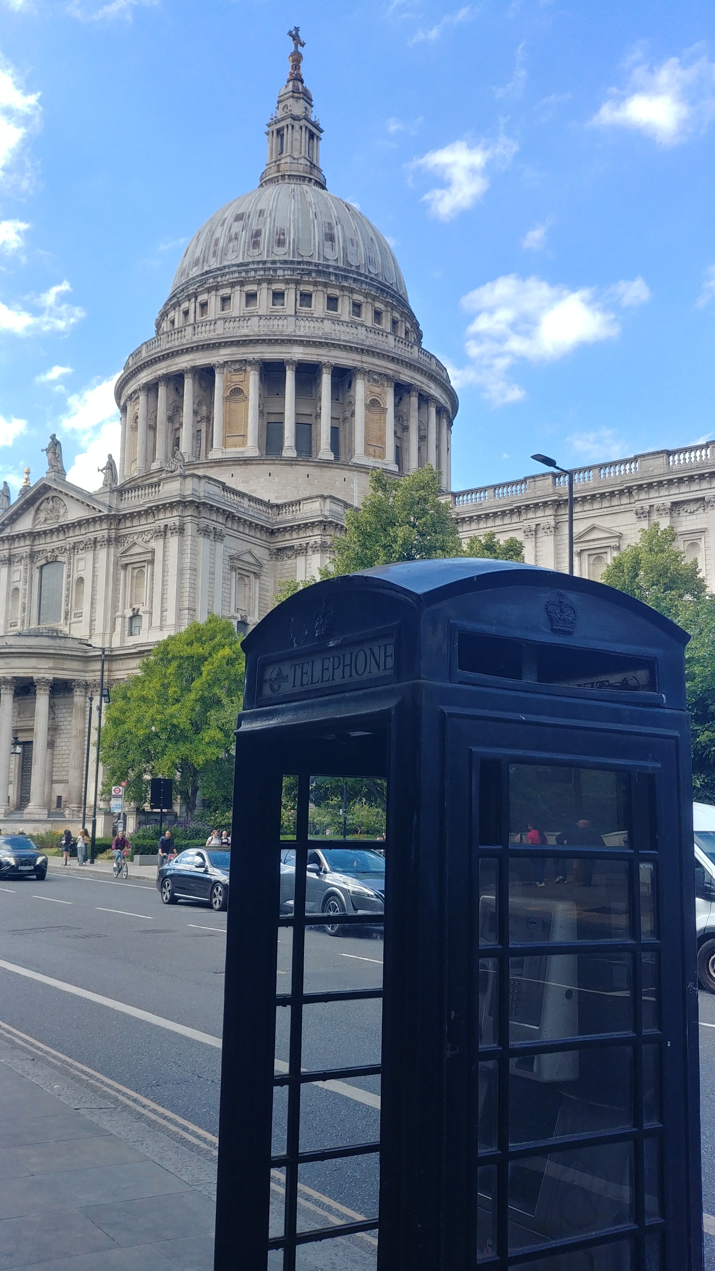 The grey dome of St Paul's Cathedral and its stone portico under blue sky, seen from the street with a black telephone box in the foreground
