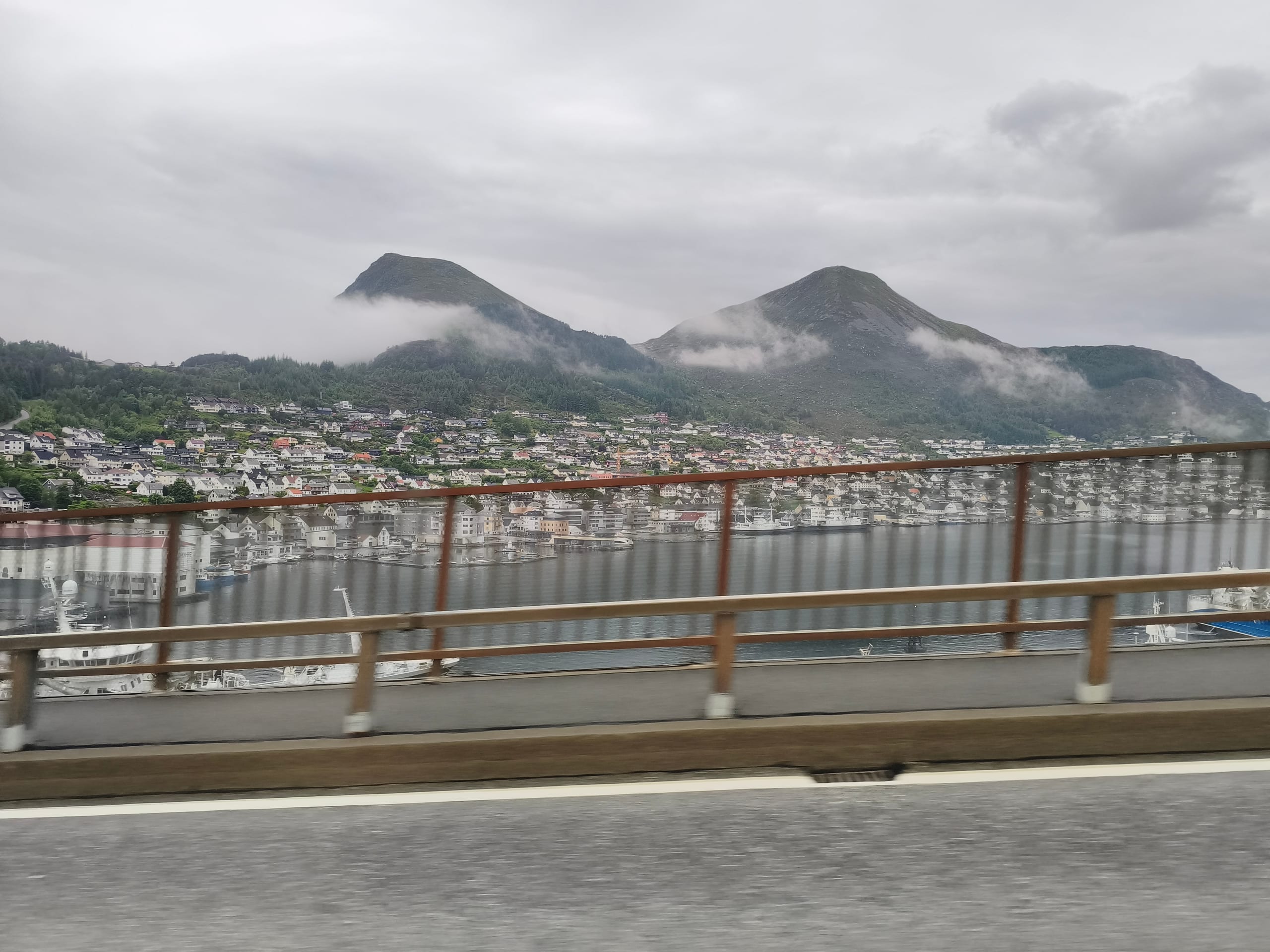 View from Måløy Bridge over the harbour town, docks, and cloud-wrapped mountains beyond the water