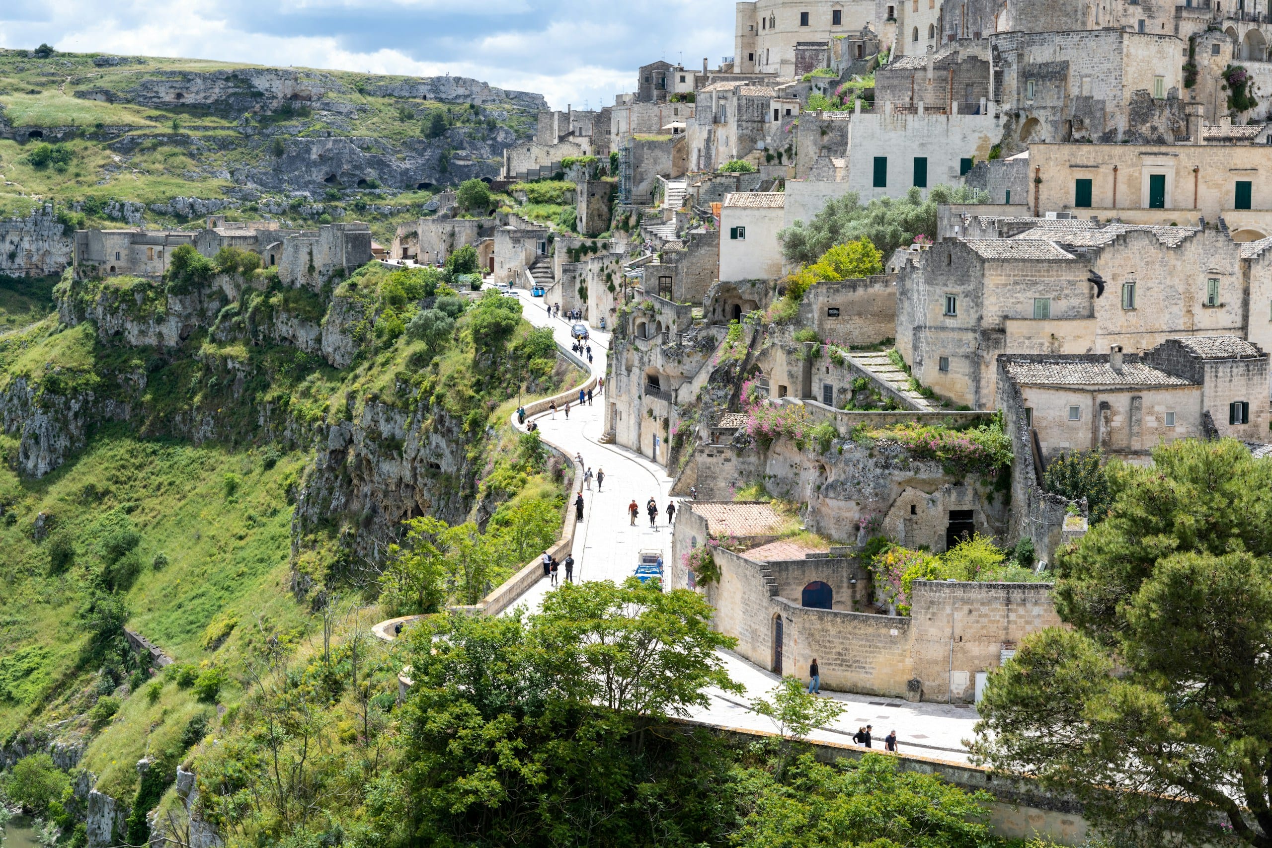 Matera's Sassi stone houses stacked above the green Gravina canyon with a winding pedestrian path through the old town