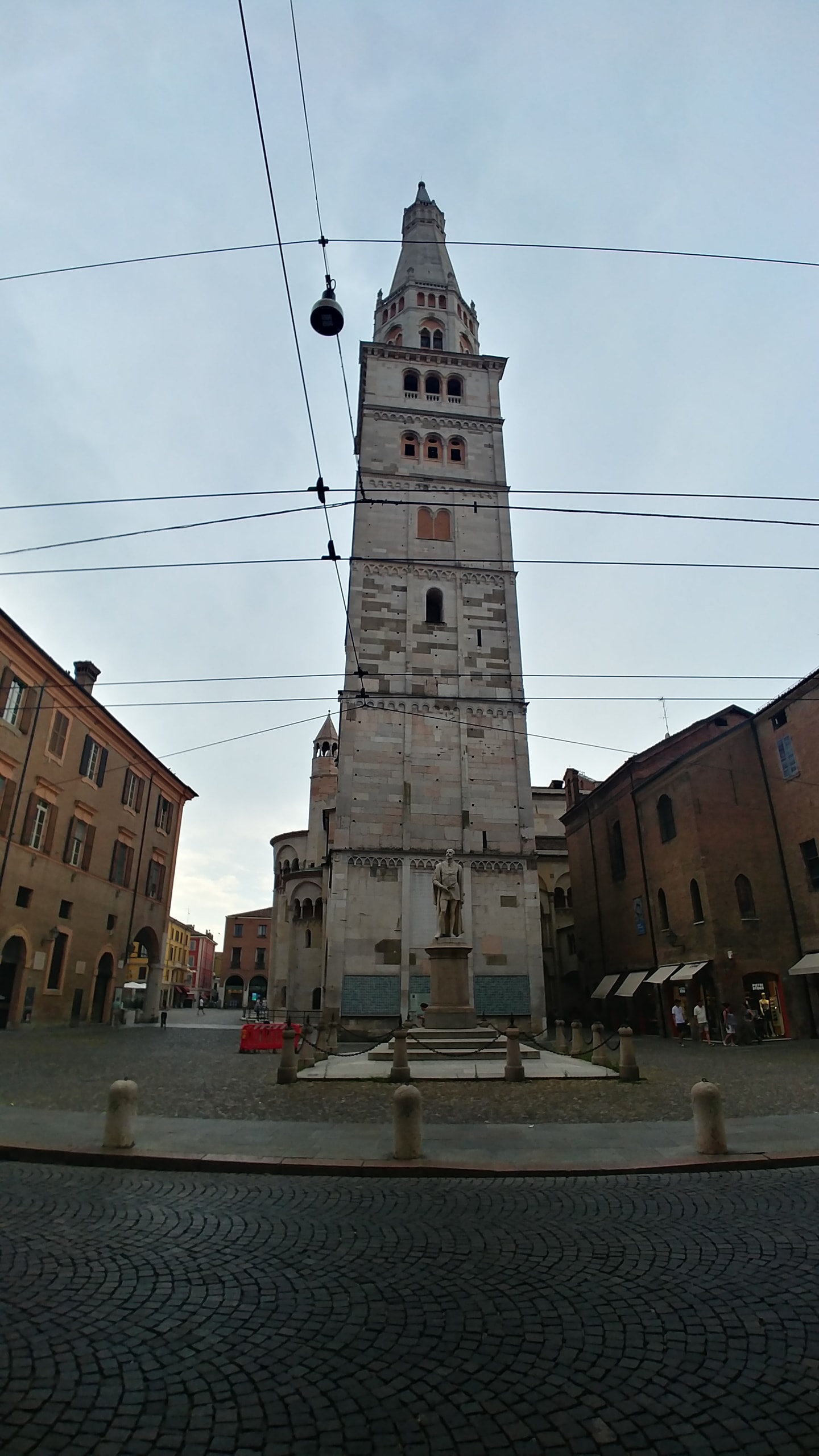 The Ghirlandina, Modena's tall white stone bell tower with a pointed spire, and the statue of the poet Alessandro Tassoni on a pedestal at its base