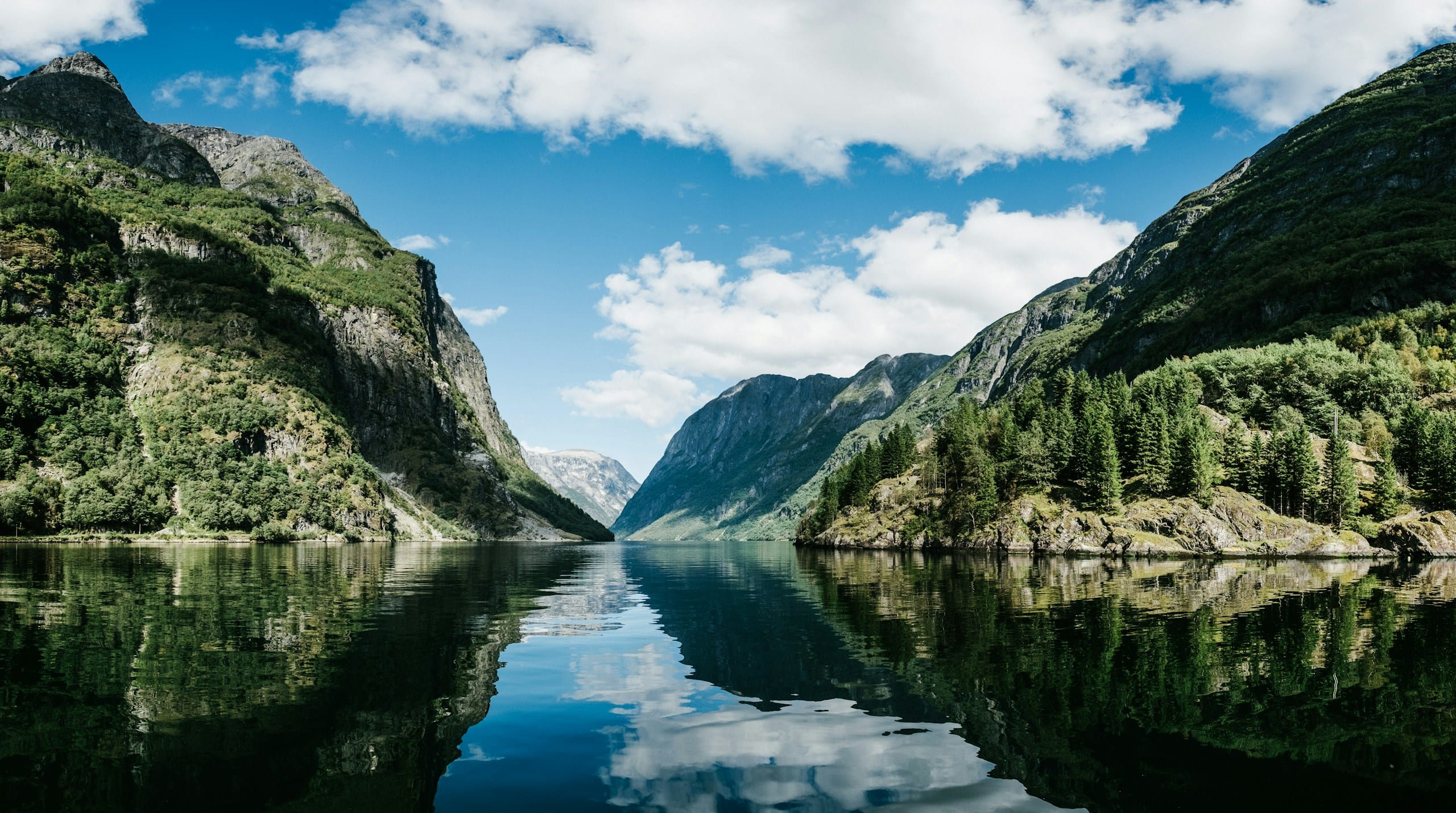 A narrow fjord near Gudvangen with steep green mountains under a ceiling of white cloud