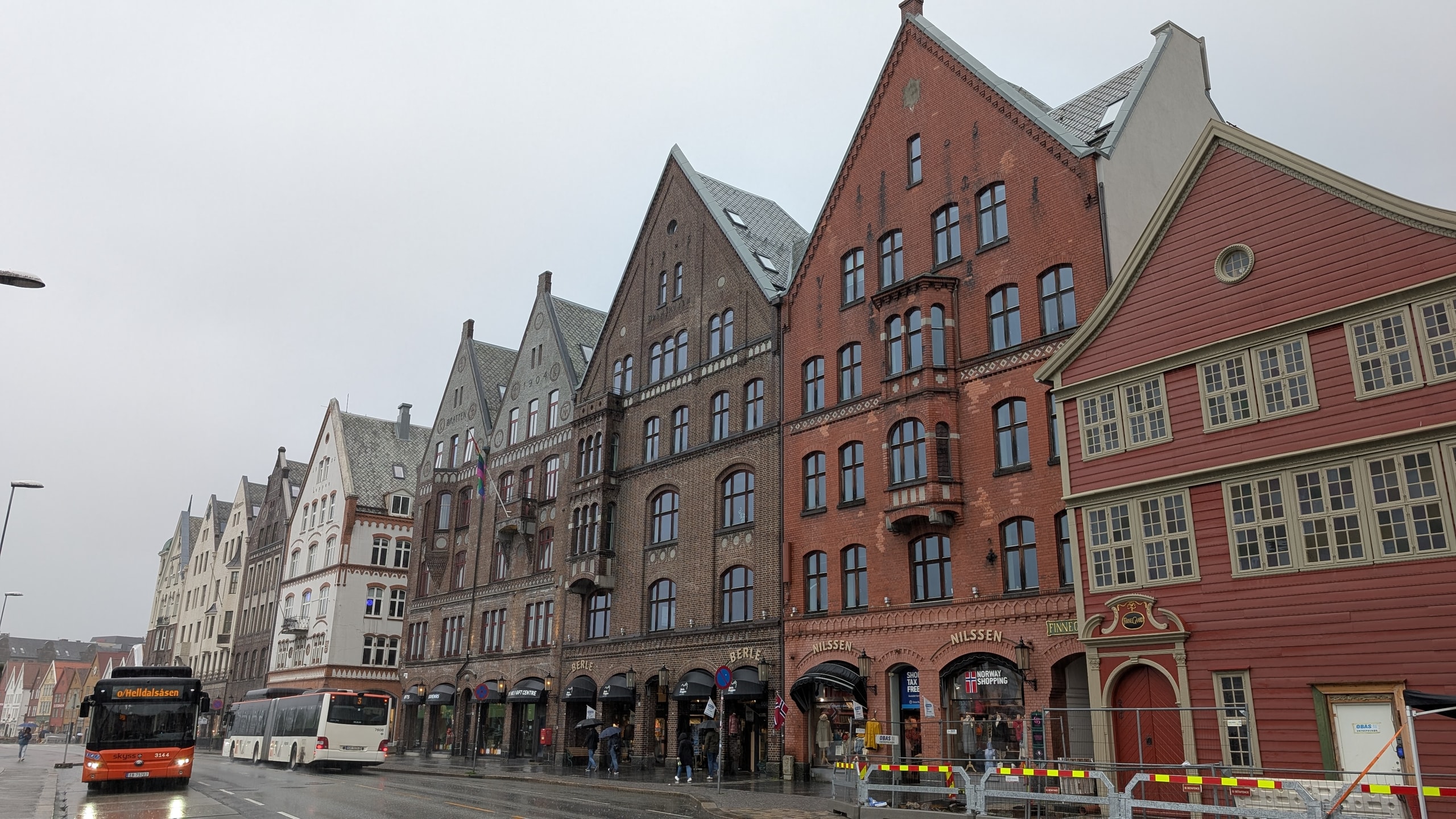Wet Bergen street with gabled wooden and brick buildings and an orange city bus under a grey sky