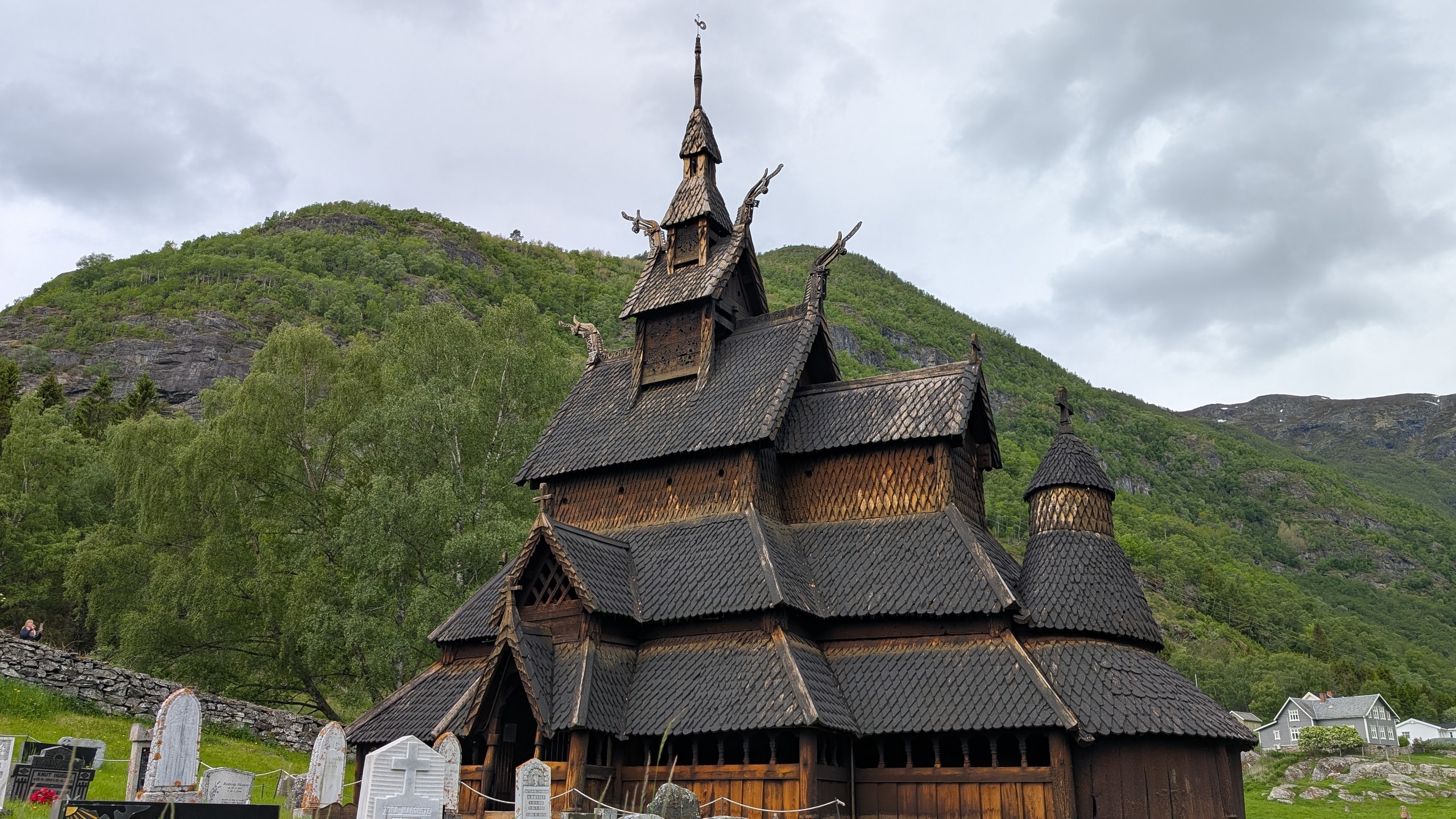 Borgund stave church with dark shingled roofs and dragon-head gables against green mountains under cloud