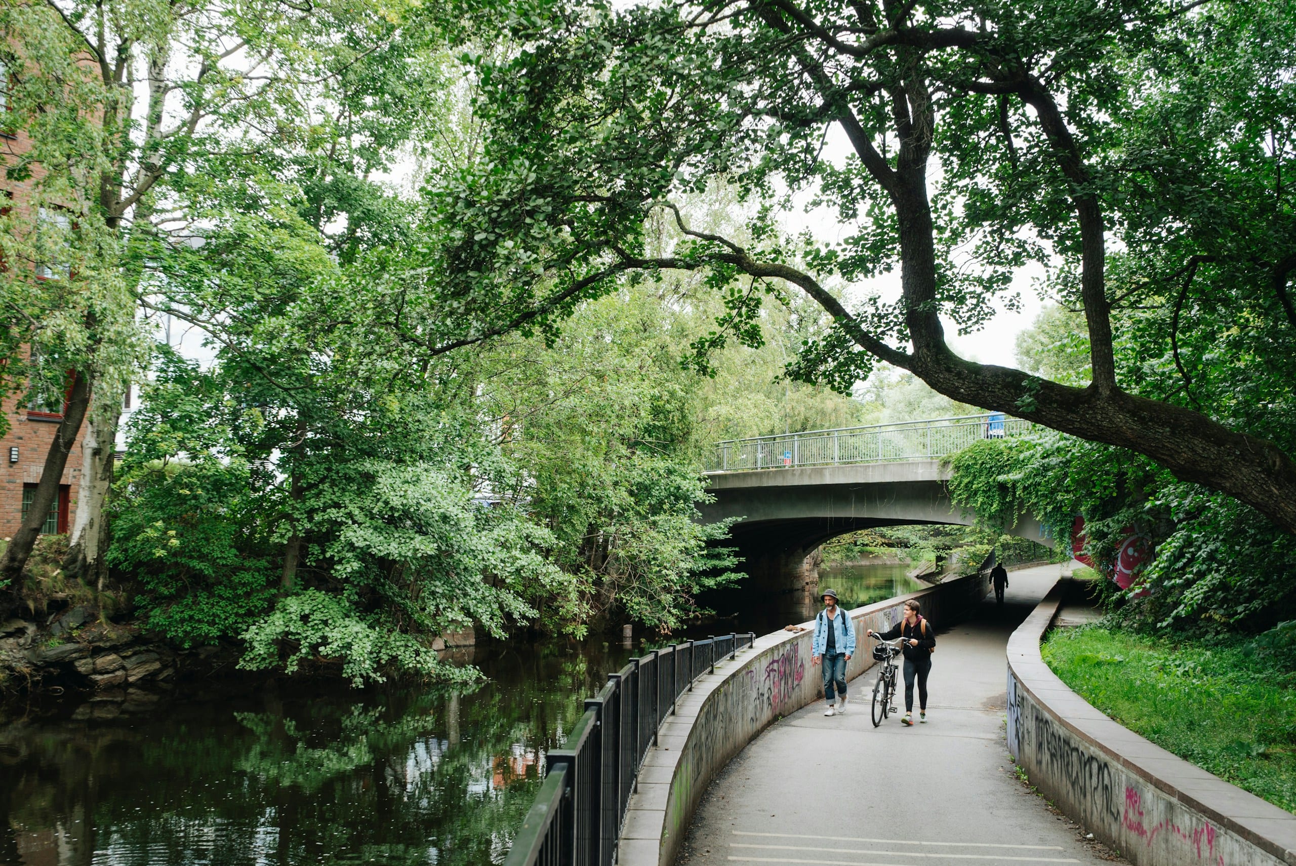 A tree-lined walking path beside the Akerselva river in Oslo with people strolling in autumn light