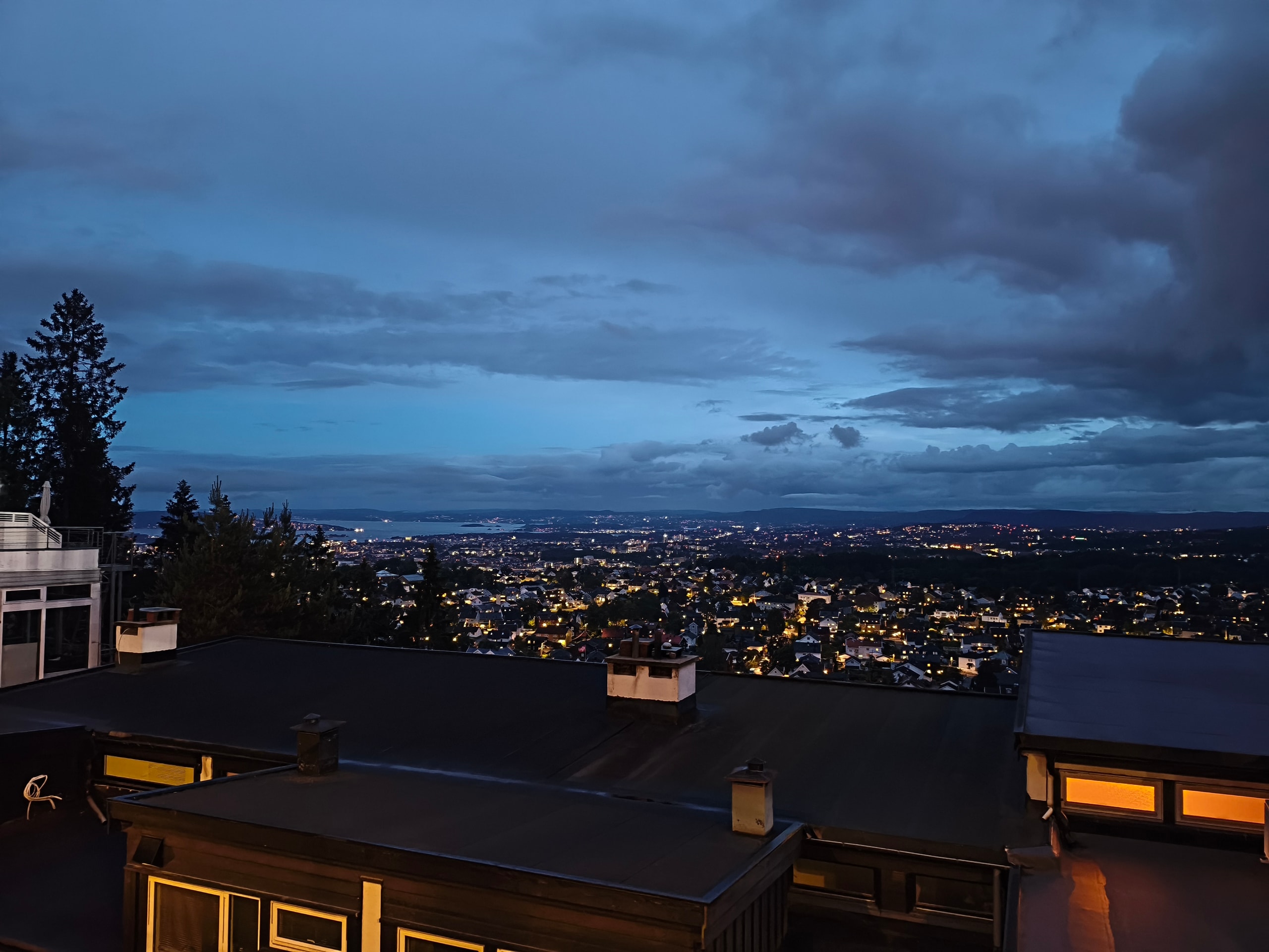 Oslo’s residential hills and fjord lights at blue hour under a heavy grey sky