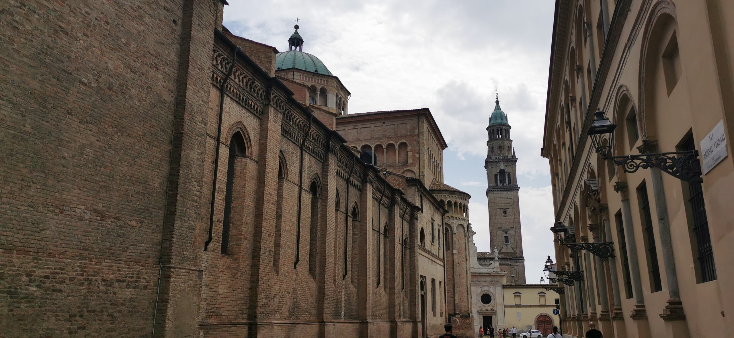 The long brick side of Parma Cathedral with its green-roofed dome, and the tall bell tower of San Giovanni Evangelista at the end of Via Cardinal Ferrari