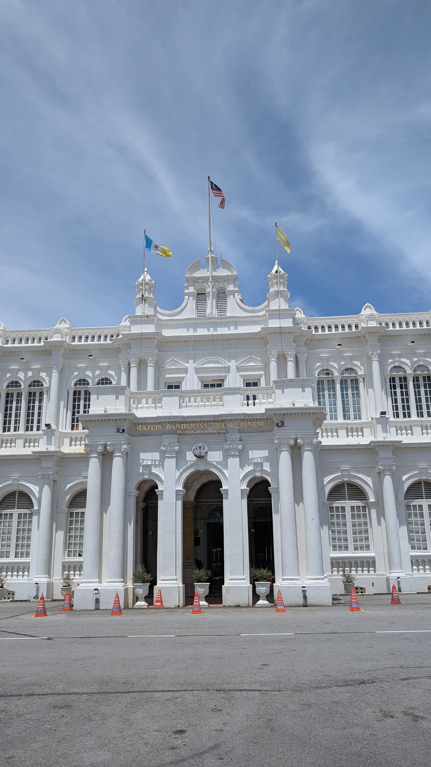 White neoclassical Penang City Hall facade with columns, gold lettering, and Malaysian and Penang flags under a clear blue sky