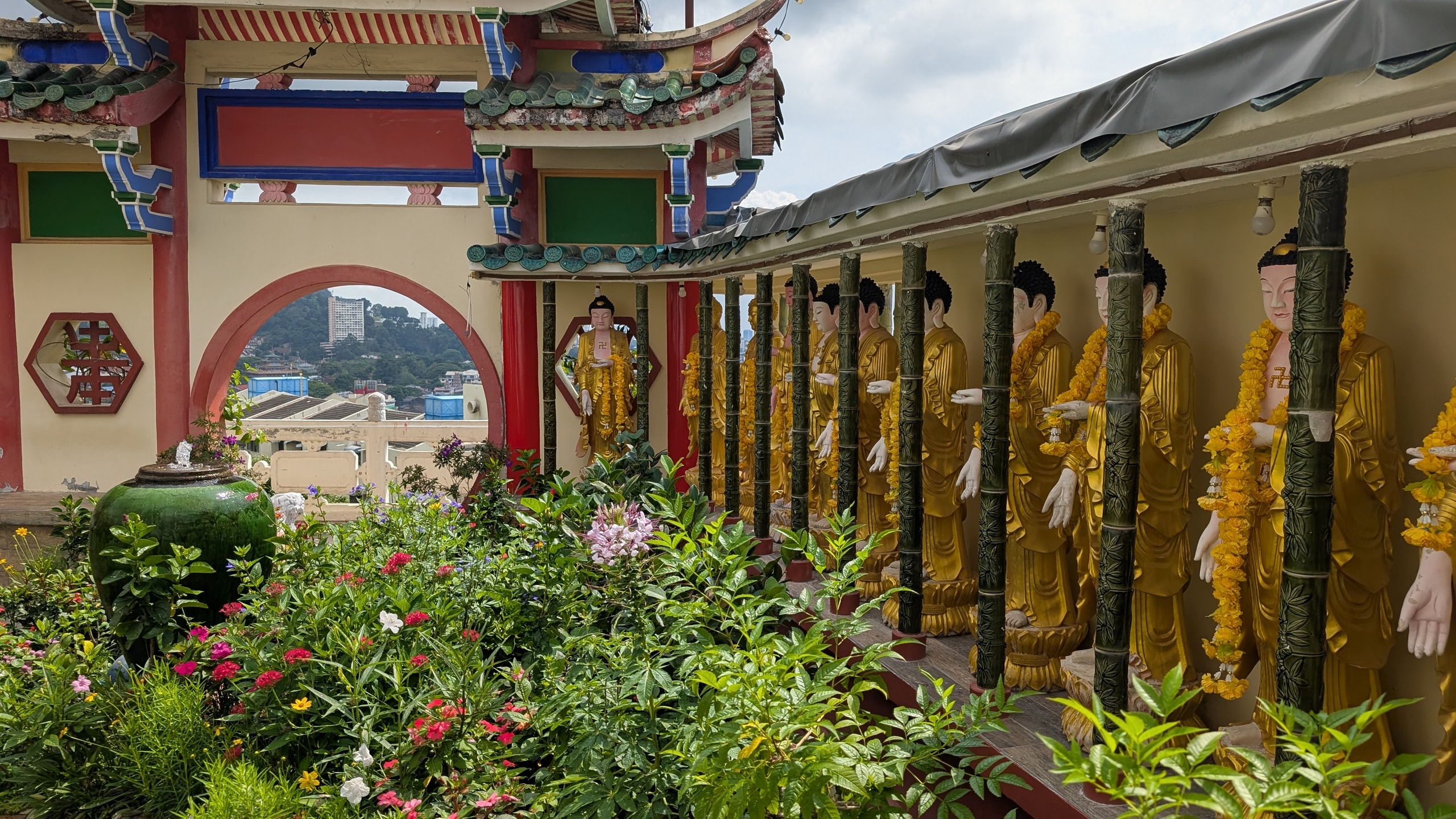 Long row of golden standing Buddha statues with yellow flower garlands under a covered walkway at Kek Lok Si Temple