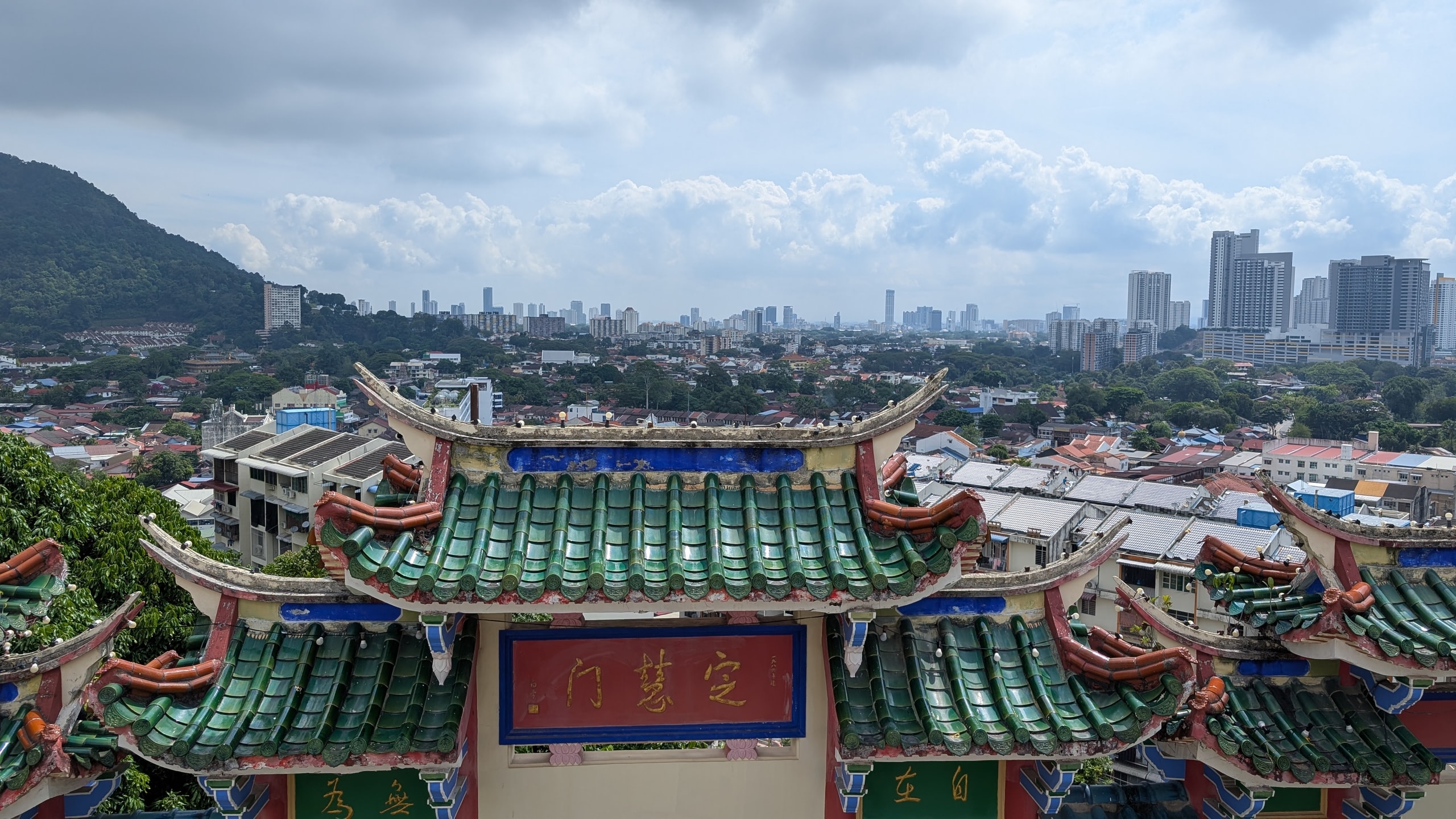 Green-tiled Chinese temple roof in the foreground overlooking suburban Penang and the George Town skyline