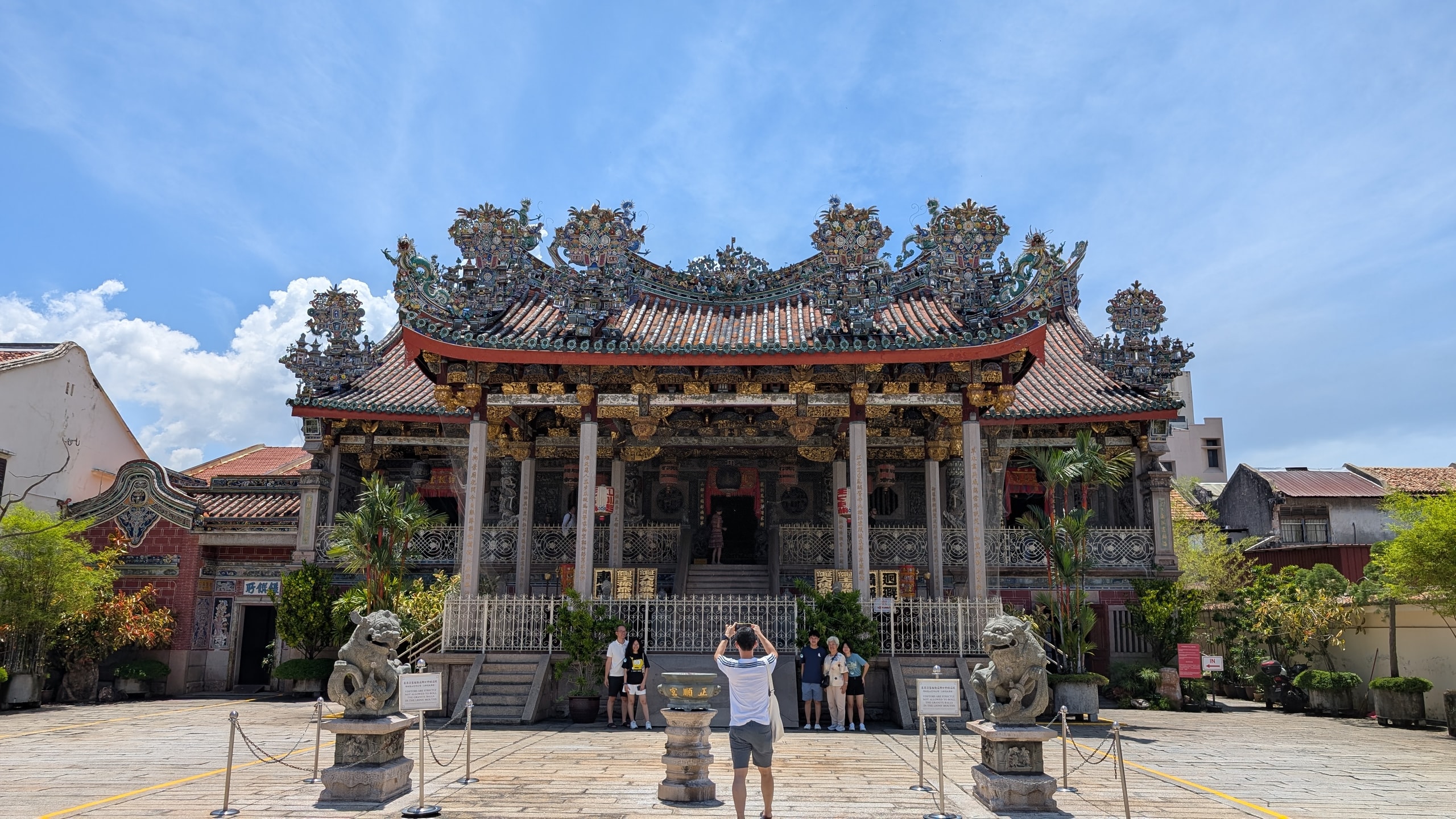 Ornate multi-tiered roof and stone courtyard of Leong San Tong Khoo Kongsi under a clear blue sky in George Town