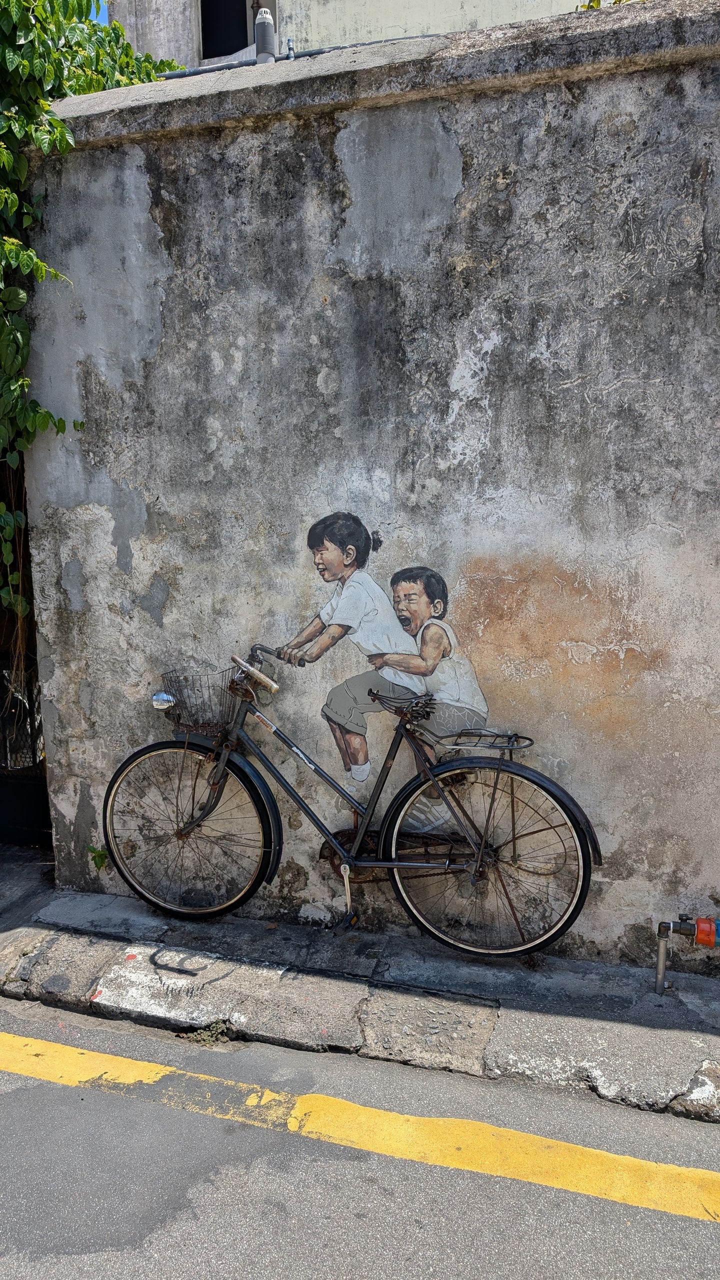Ernest Zacharevic mural of two children painted as if riding a real vintage bicycle against a weathered George Town wall