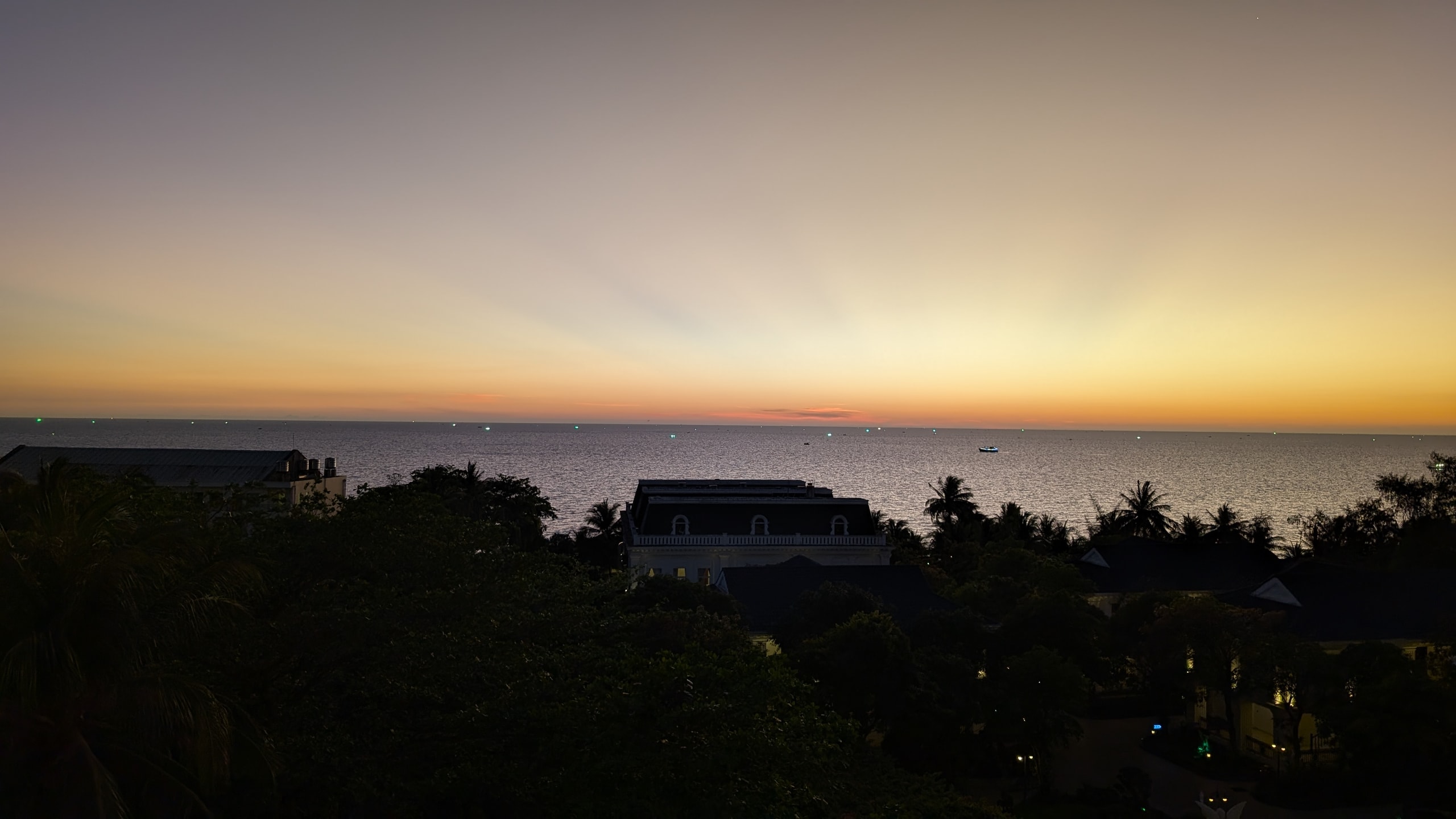 Dusk over a flat sea with an orange band on the horizon and small green lights from squid fishing boats offshore