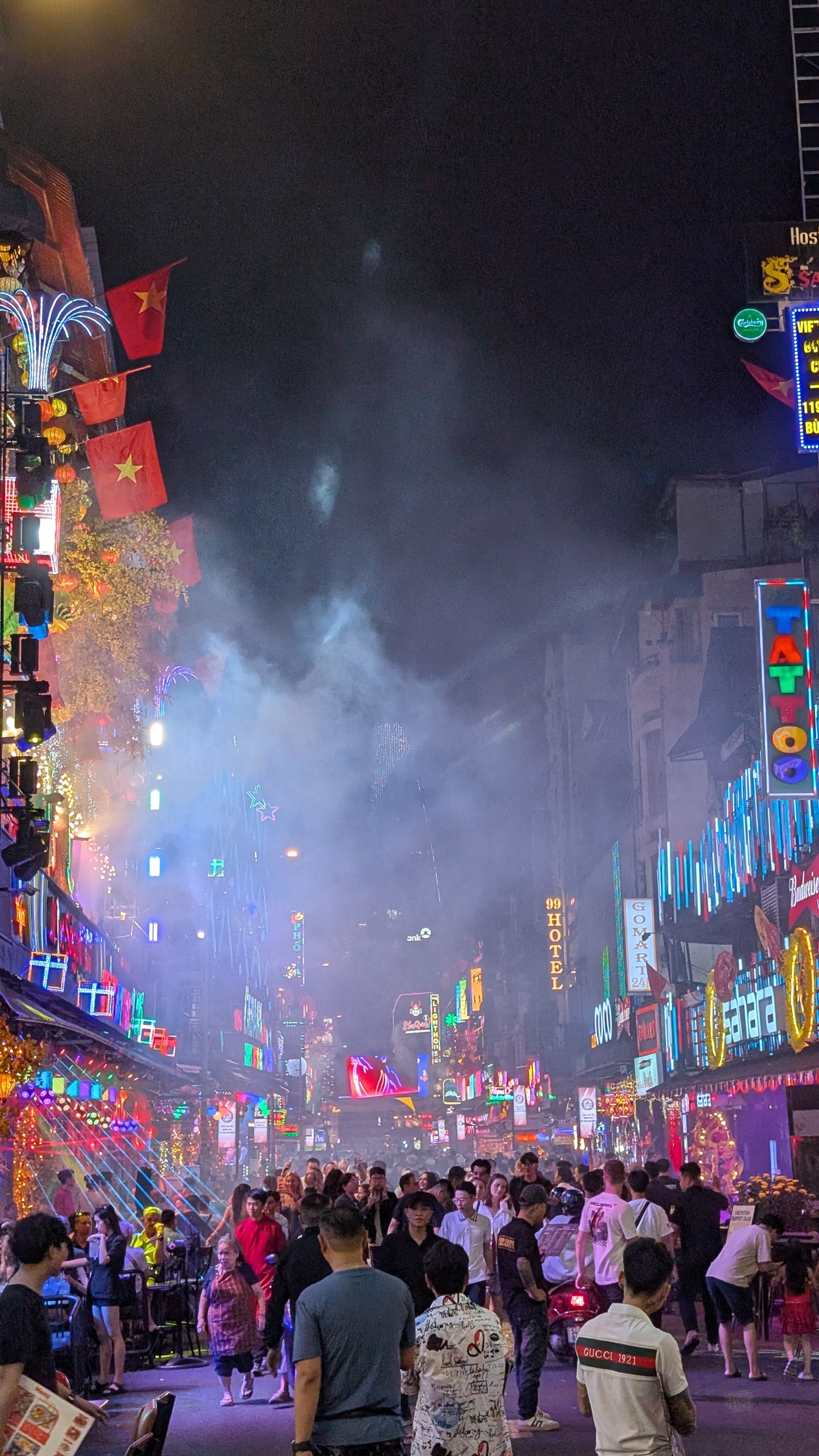 Crowded Bui Vien Walking Street at night with neon signs, smoke, and people packed between lit buildings