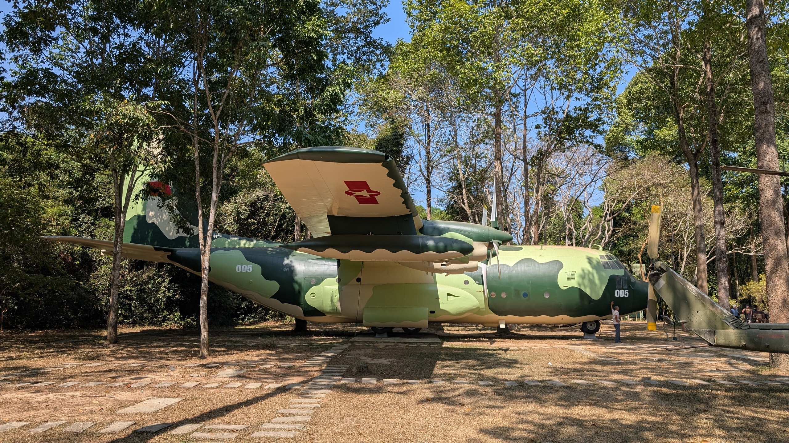 A camouflage Fairchild C-123 military transport plane marked 005 in a clearing at the Cu Chi tunnels site