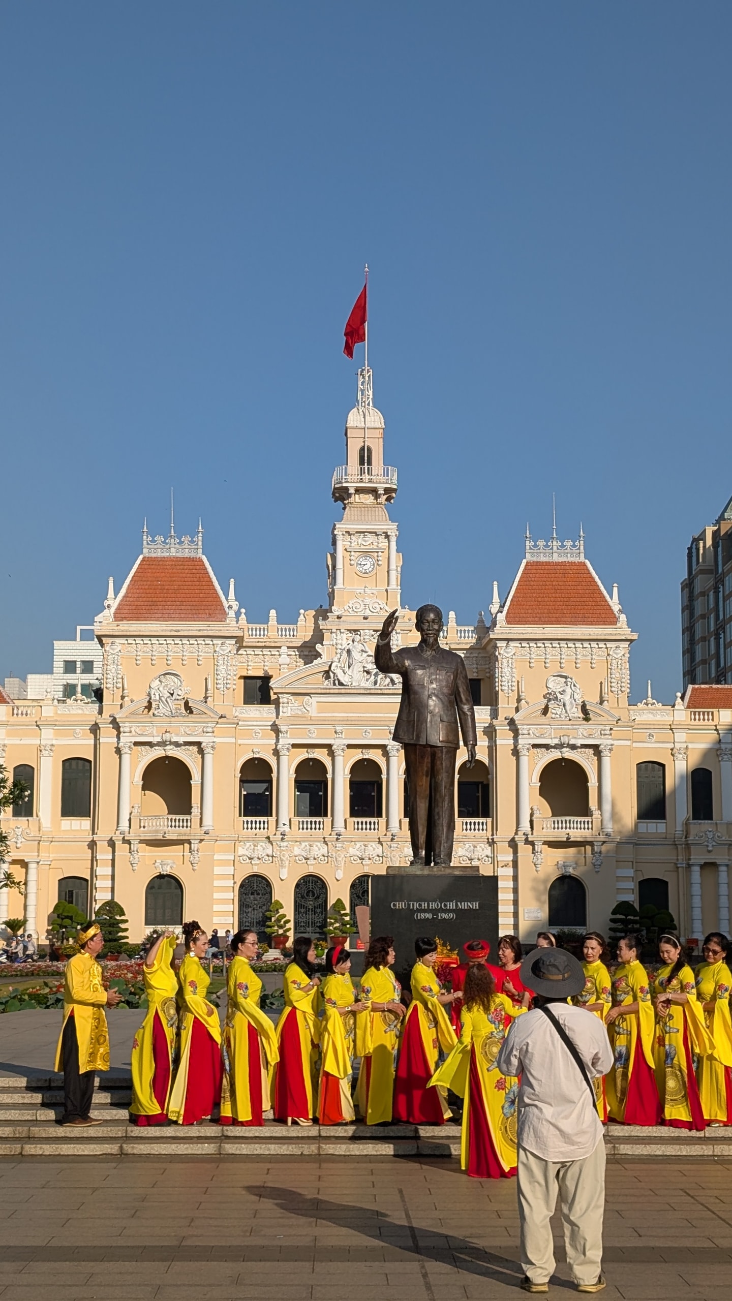 Ho Chi Minh statue in front of the People's Committee Building on Nguyen Hue, with a group in yellow ao dai posing below